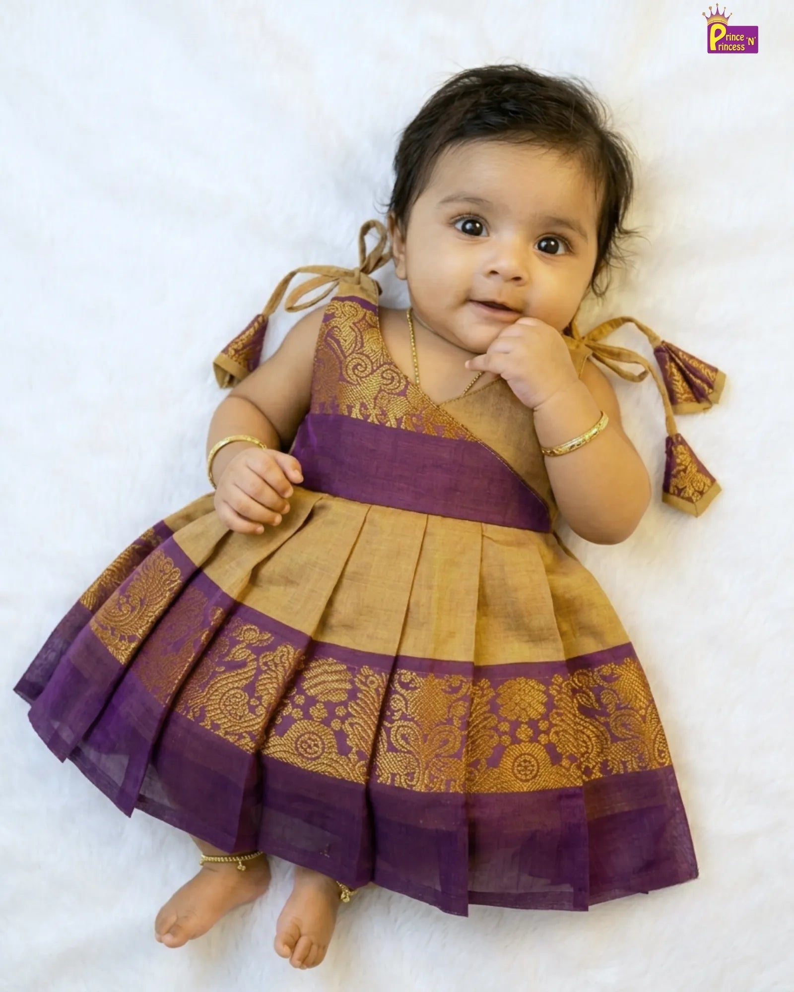 Baby wearing a traditional outfit with purple and gold colors on a white background