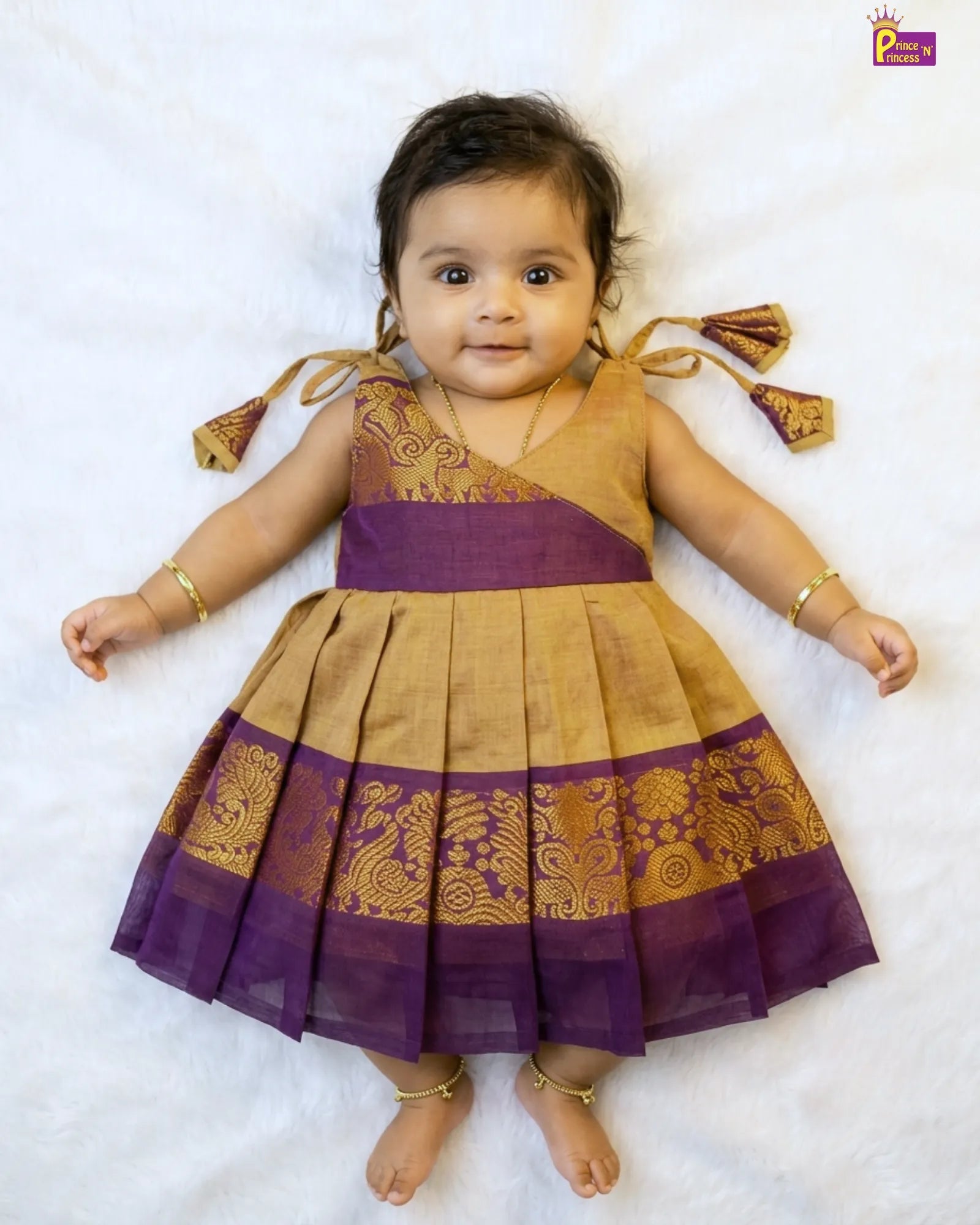 Baby wearing a traditional purple and gold dress on a white background