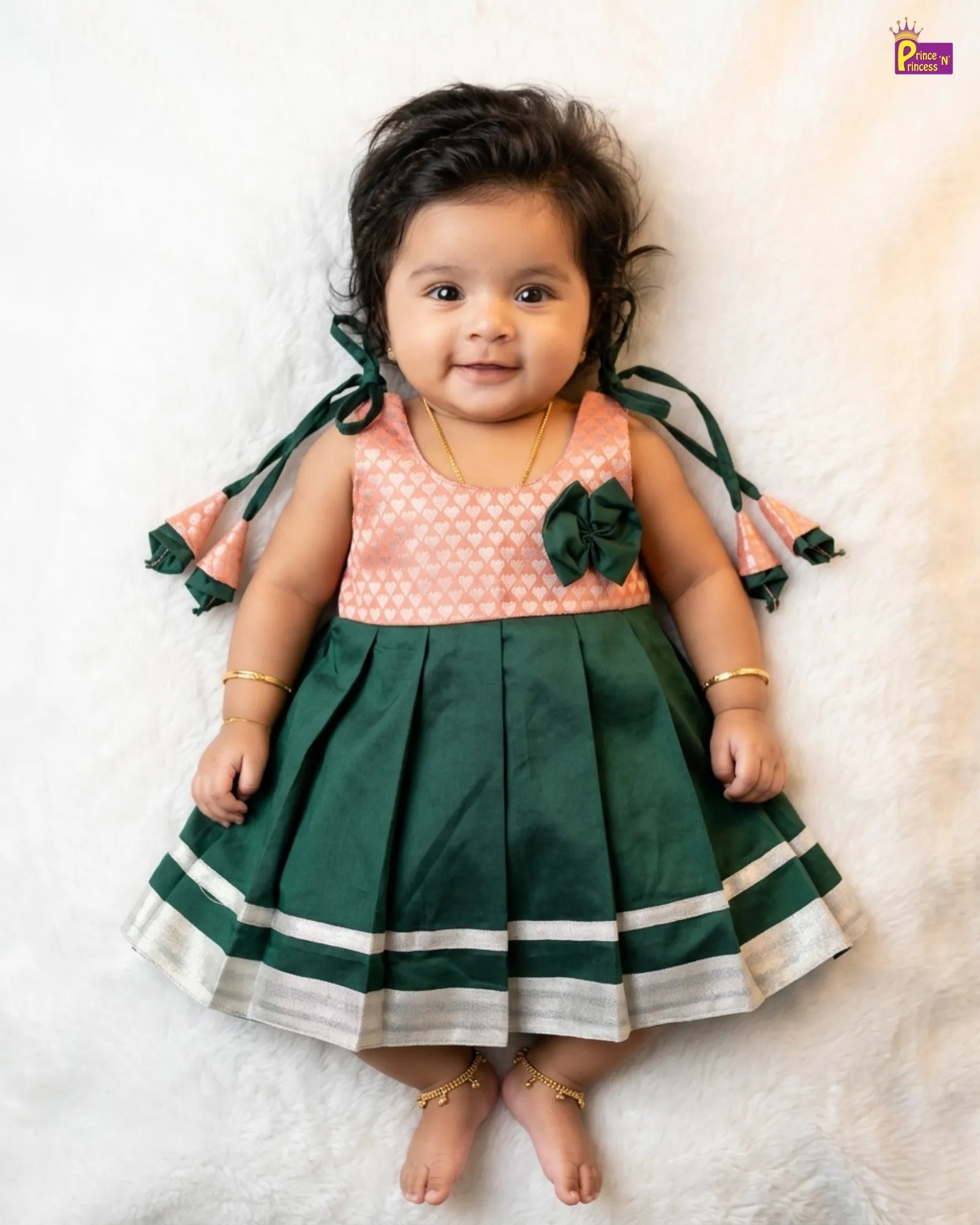 Baby wearing a green and pink dress with floral details on a white background