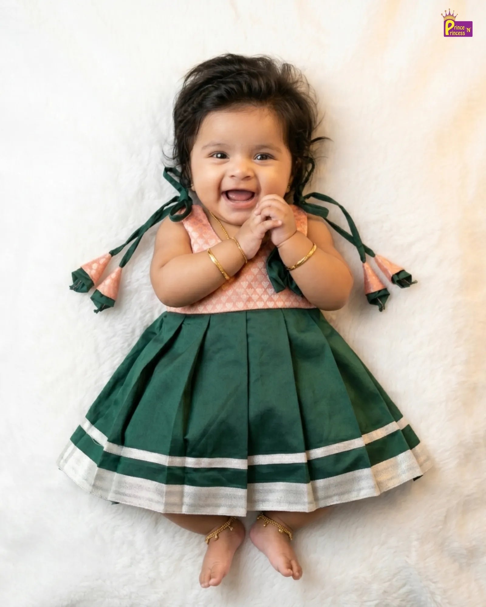 Baby wearing a green and pink dress with tassels on a white background