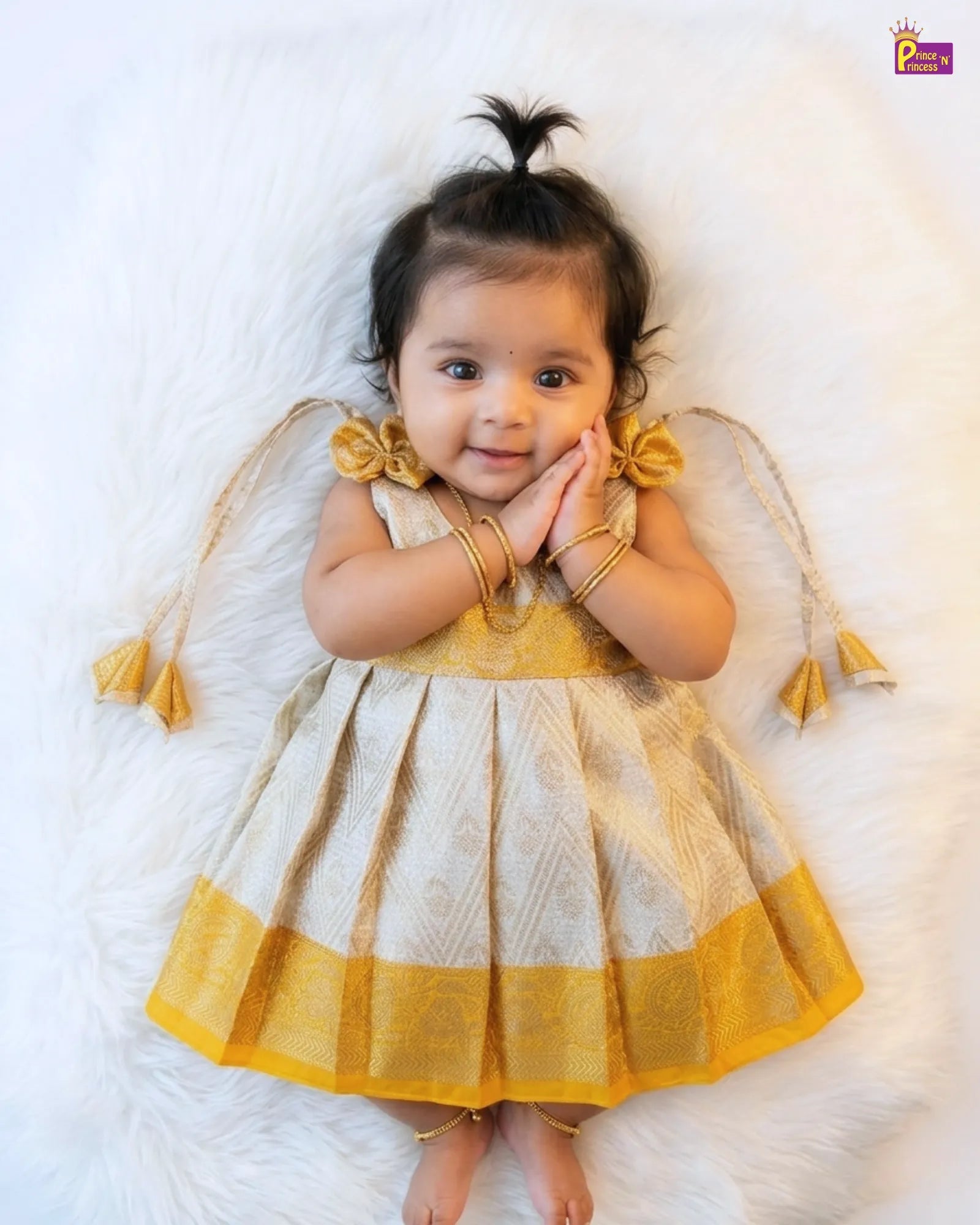 Baby wearing a yellow and white traditional outfit on a white background