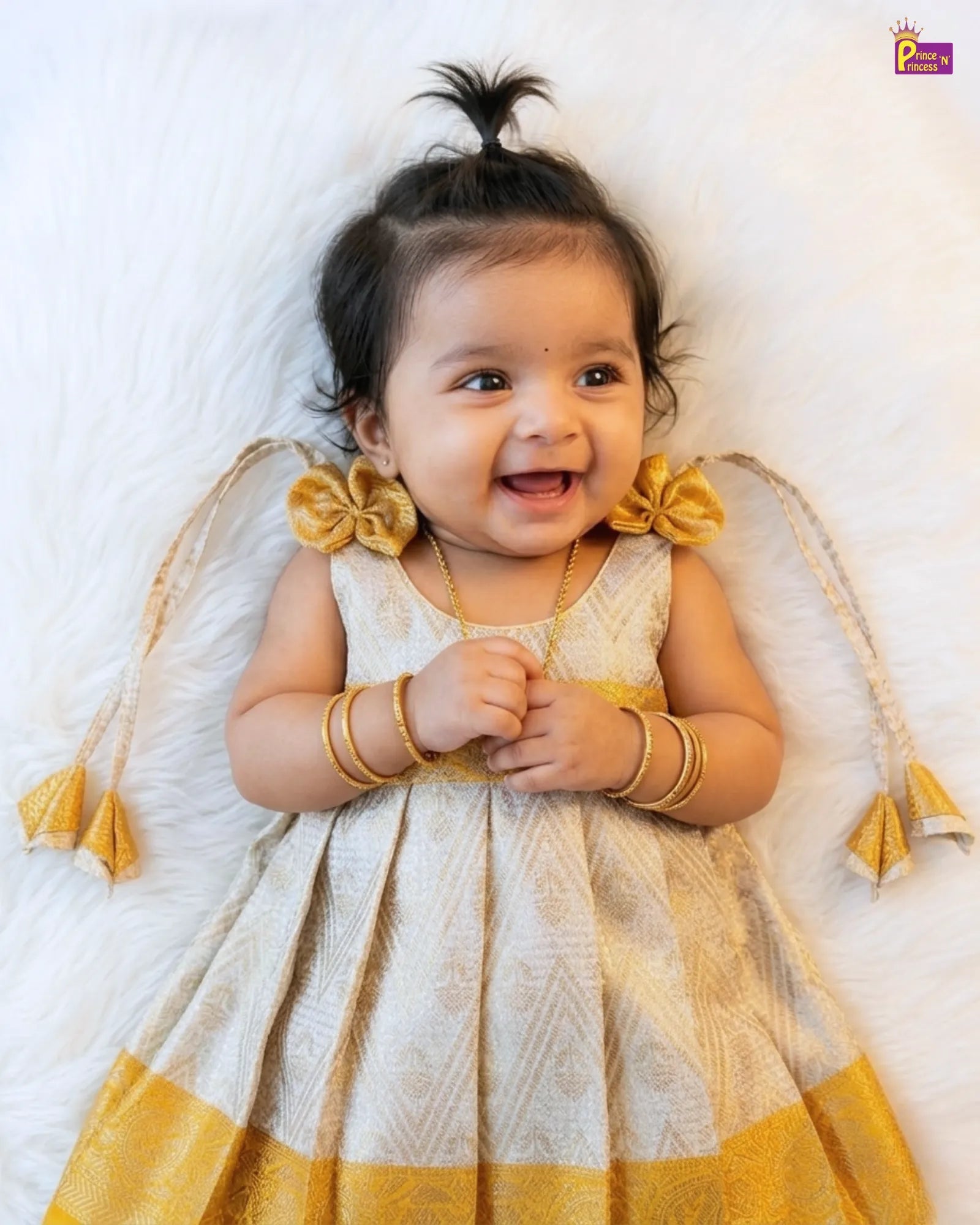 Baby in a yellow and white dress with tassels on a white background