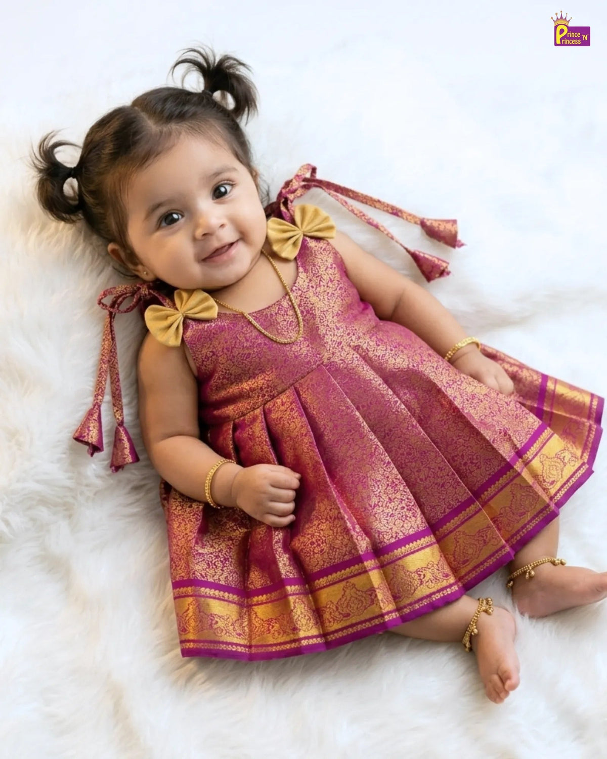 Baby girl in a pink and gold traditional outfit lying on a white surface