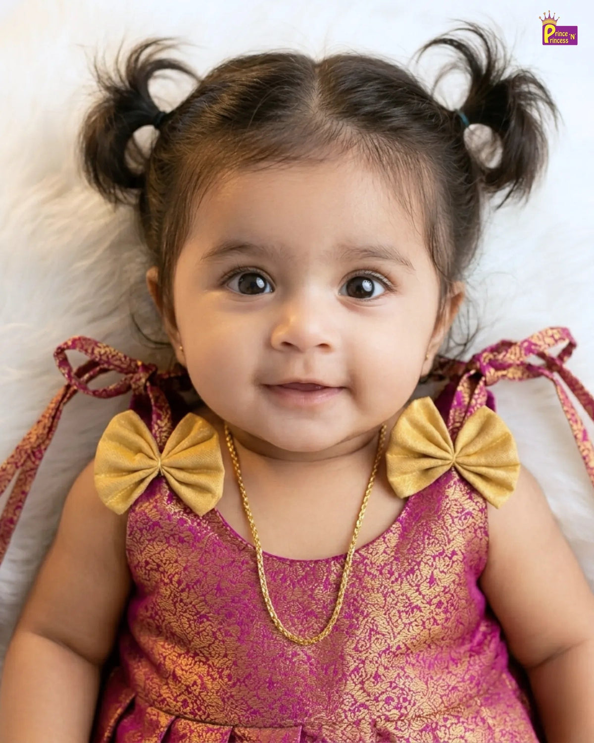 Child wearing a pink and gold traditional outfit with large yellow bows on a white background