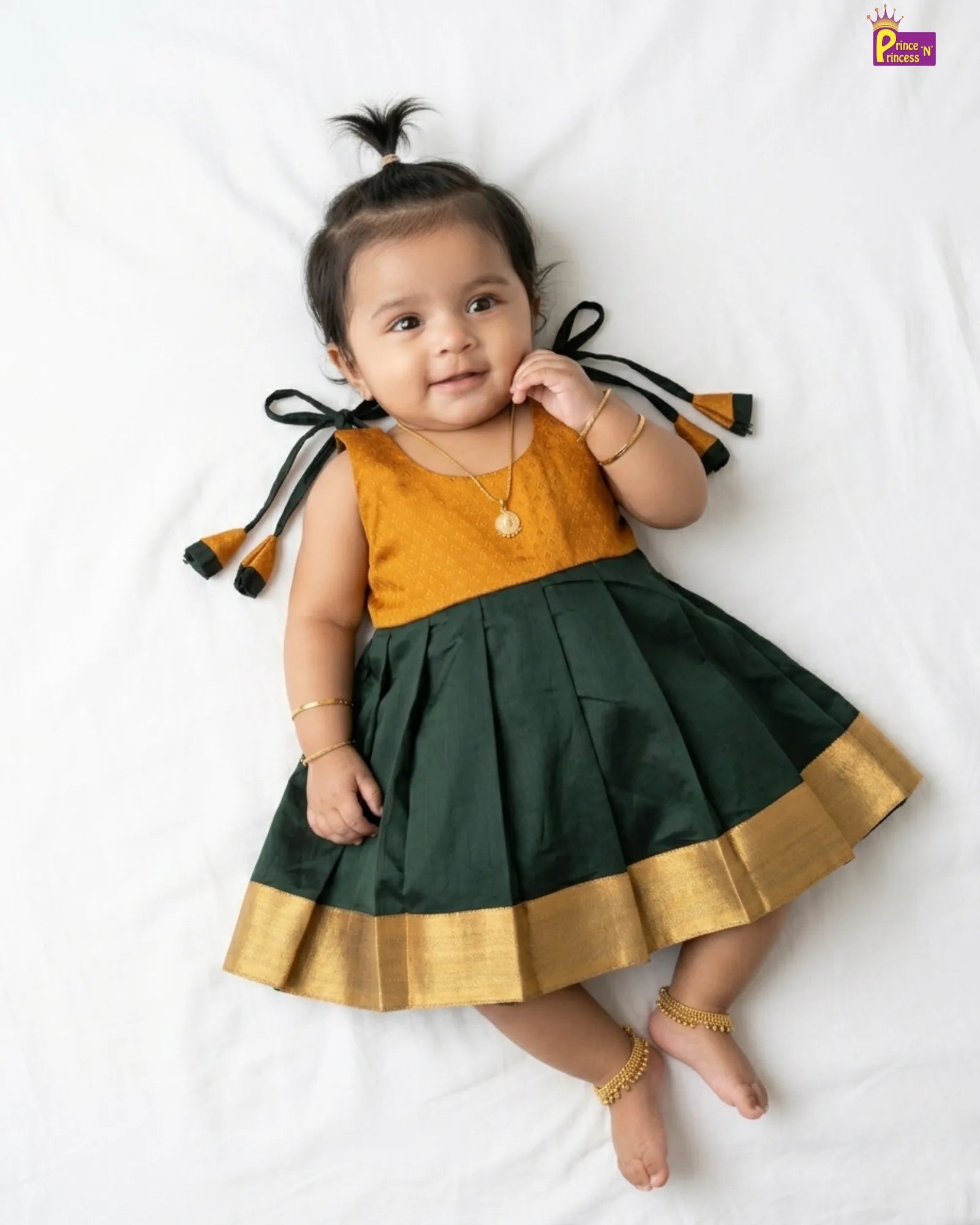 Baby wearing a green and gold traditional outfit with tassels on a white background