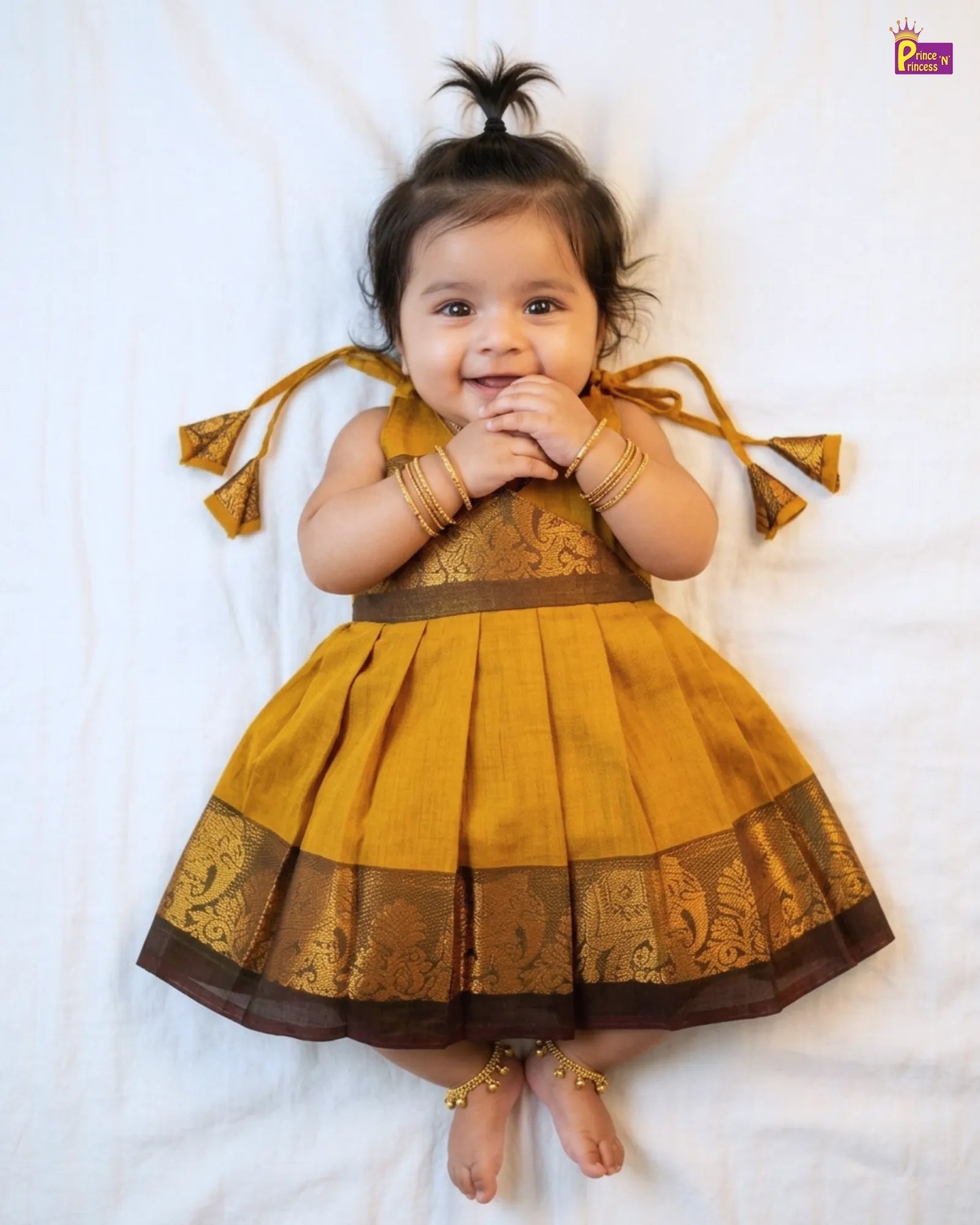 Baby wearing a traditional yellow and brown dress with decorative elements on a white background