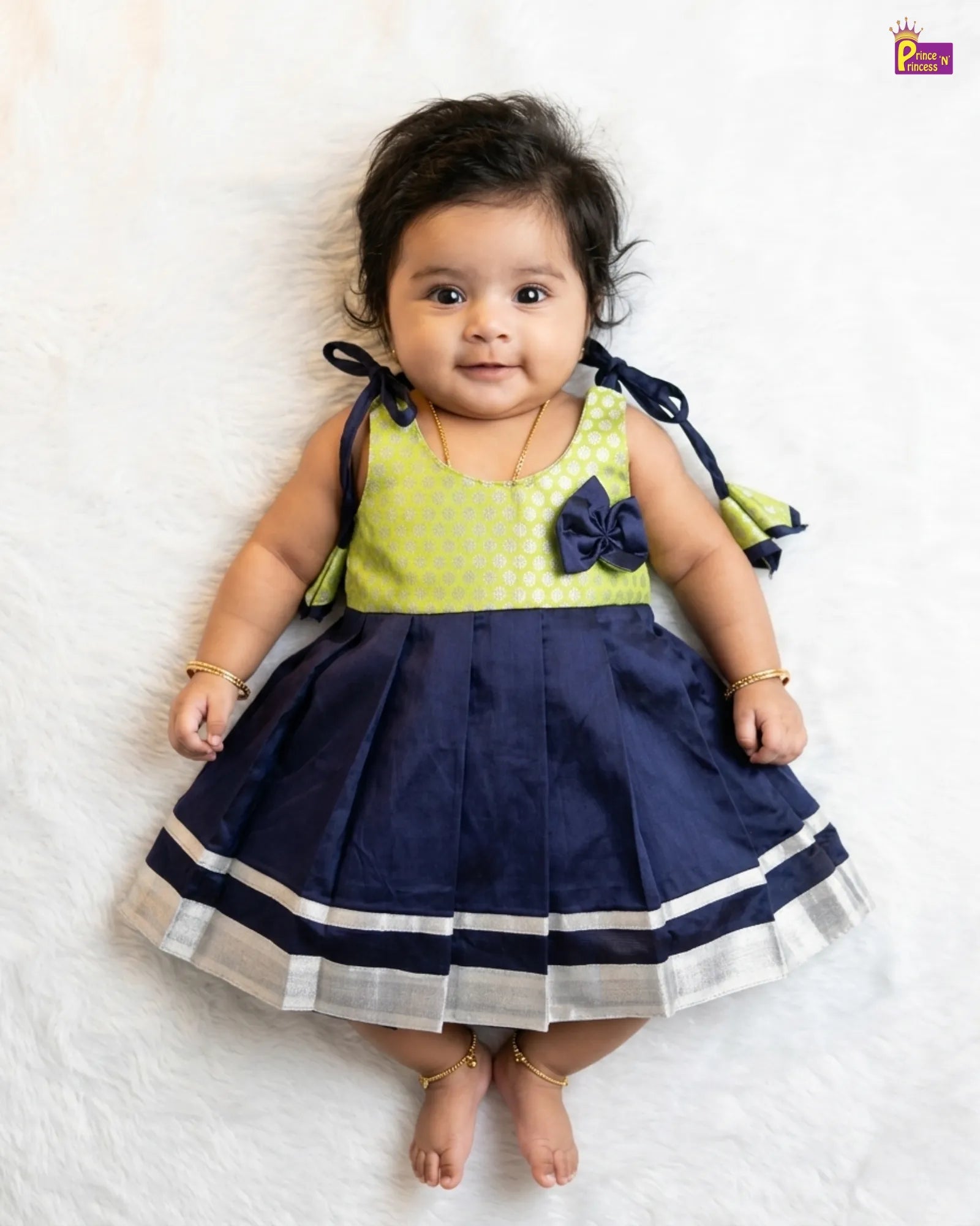 Baby wearing a green top and navy blue skirt with a bow on a white background