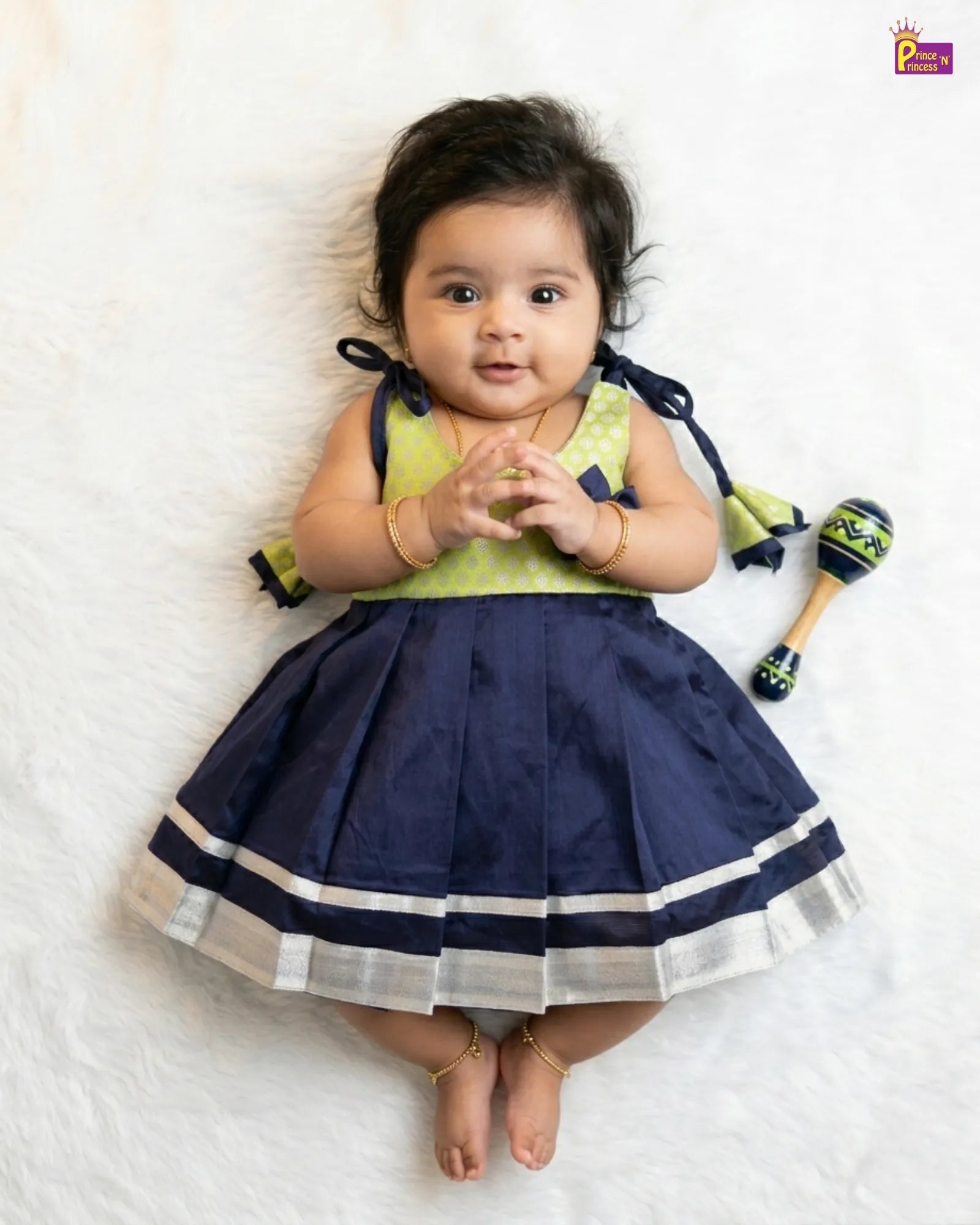 Baby wearing a navy blue and green dress with maracas on a white background