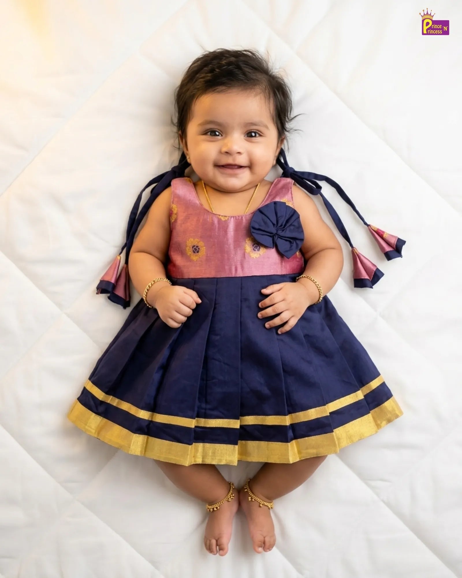 Baby wearing a pink and navy dress with a flower detail on a white background