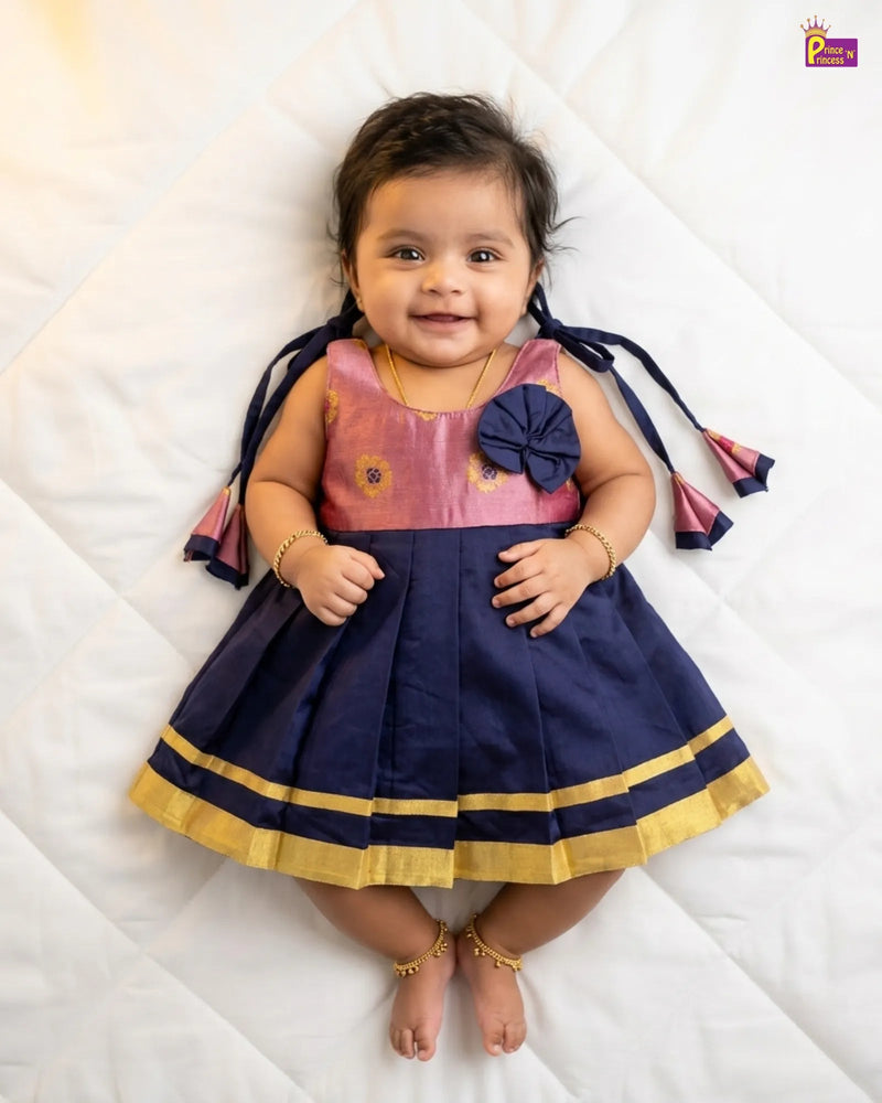 Baby wearing a pink and navy dress with a flower detail on a white background