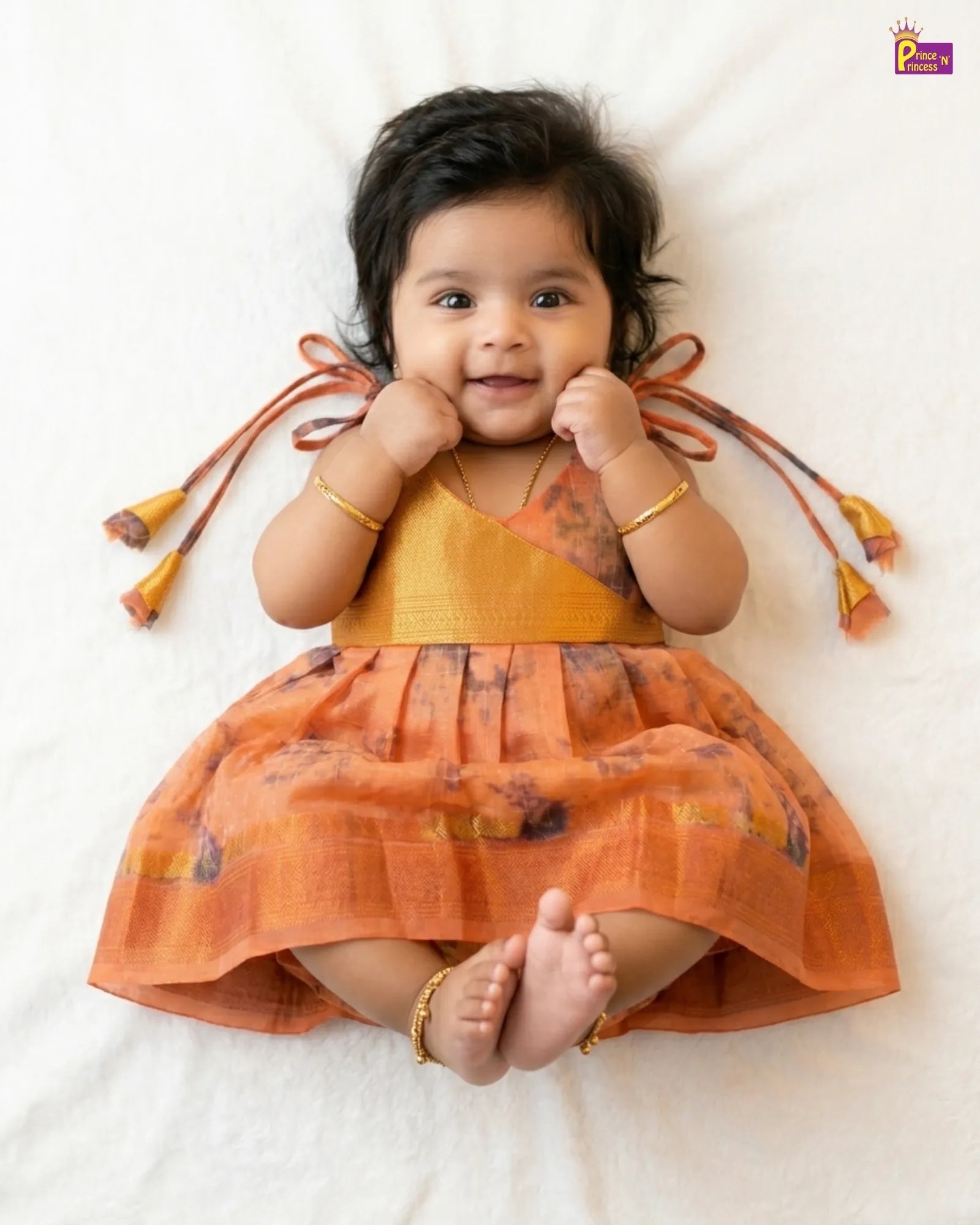 Baby wearing an orange dress with tassels on a white background
