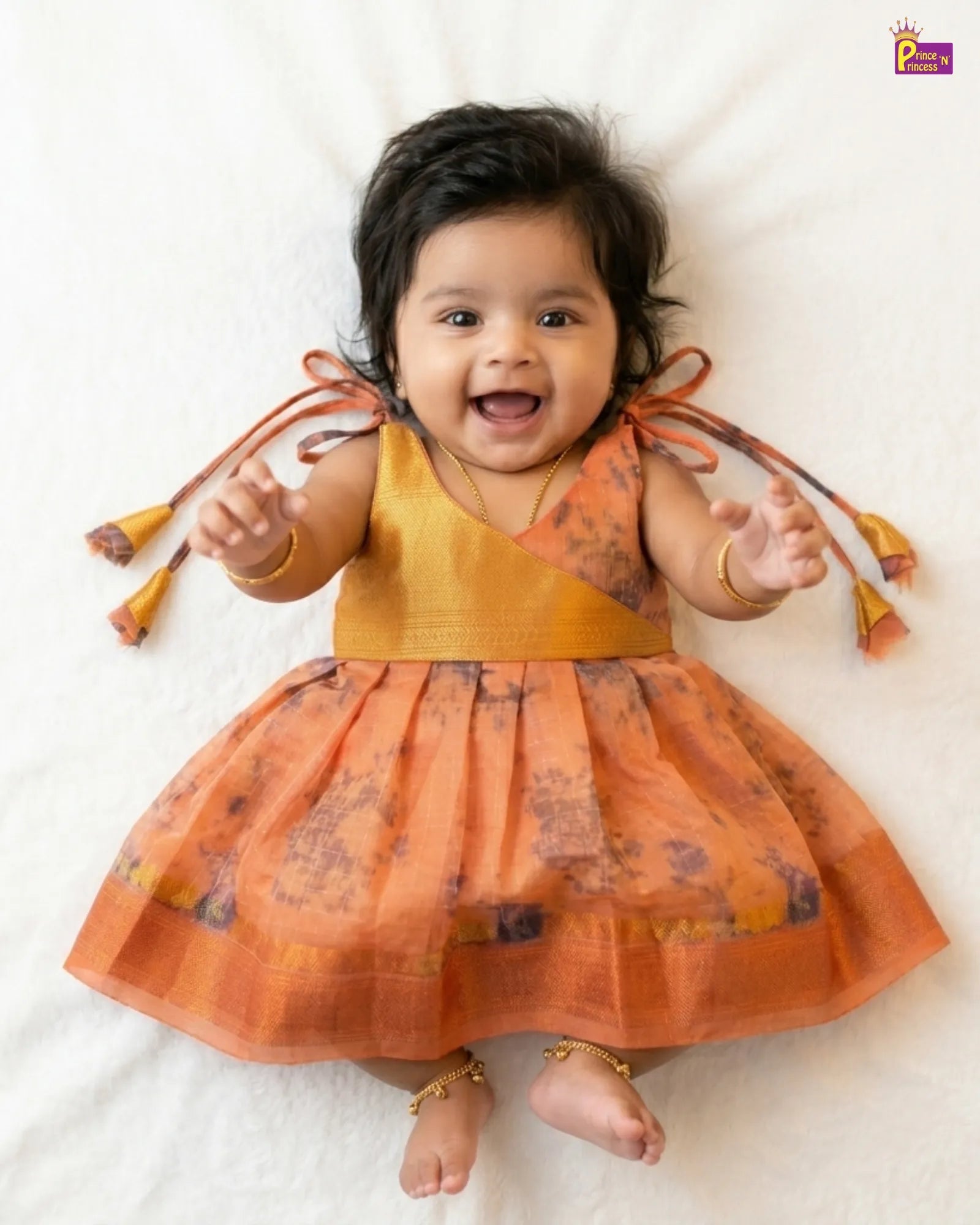 Baby wearing an orange dress with floral patterns on a white background