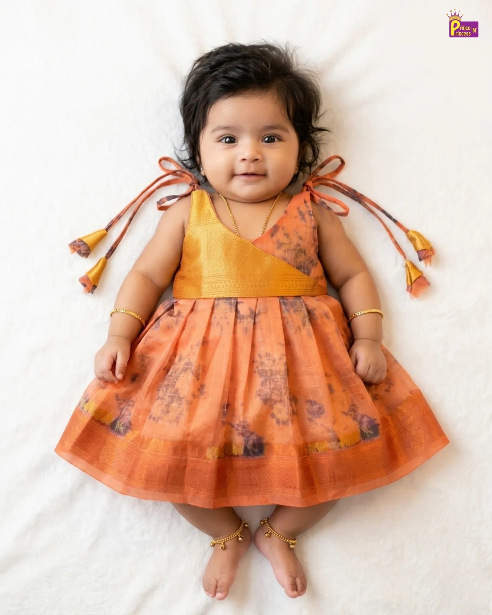 Baby wearing an orange dress with floral patterns on a white background