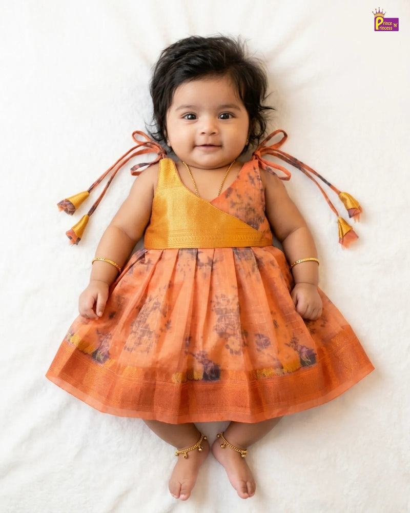 Baby wearing an orange dress with floral patterns on a white background
