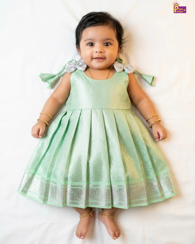 Baby wearing a light green dress with ruffled sleeves on a white background