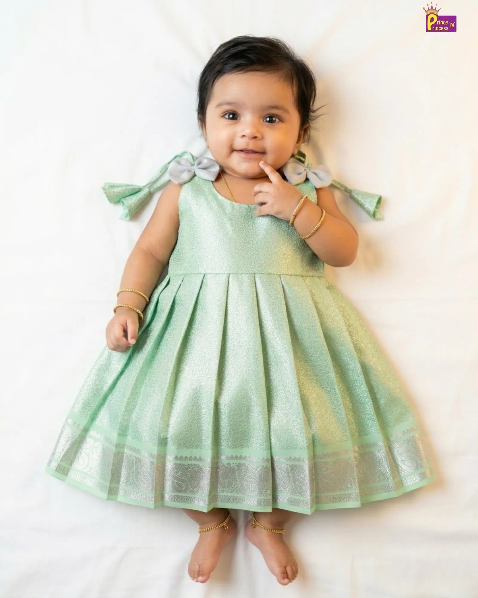 Baby wearing a light green dress with ruffled sleeves on a white background