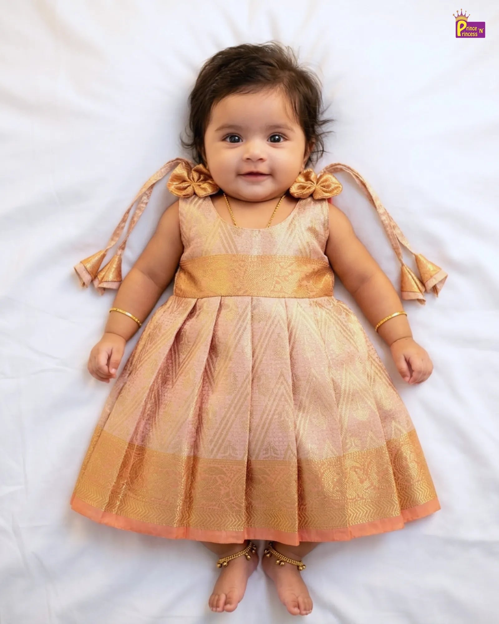 Baby wearing a traditional outfit with gold and pink colors on a white background