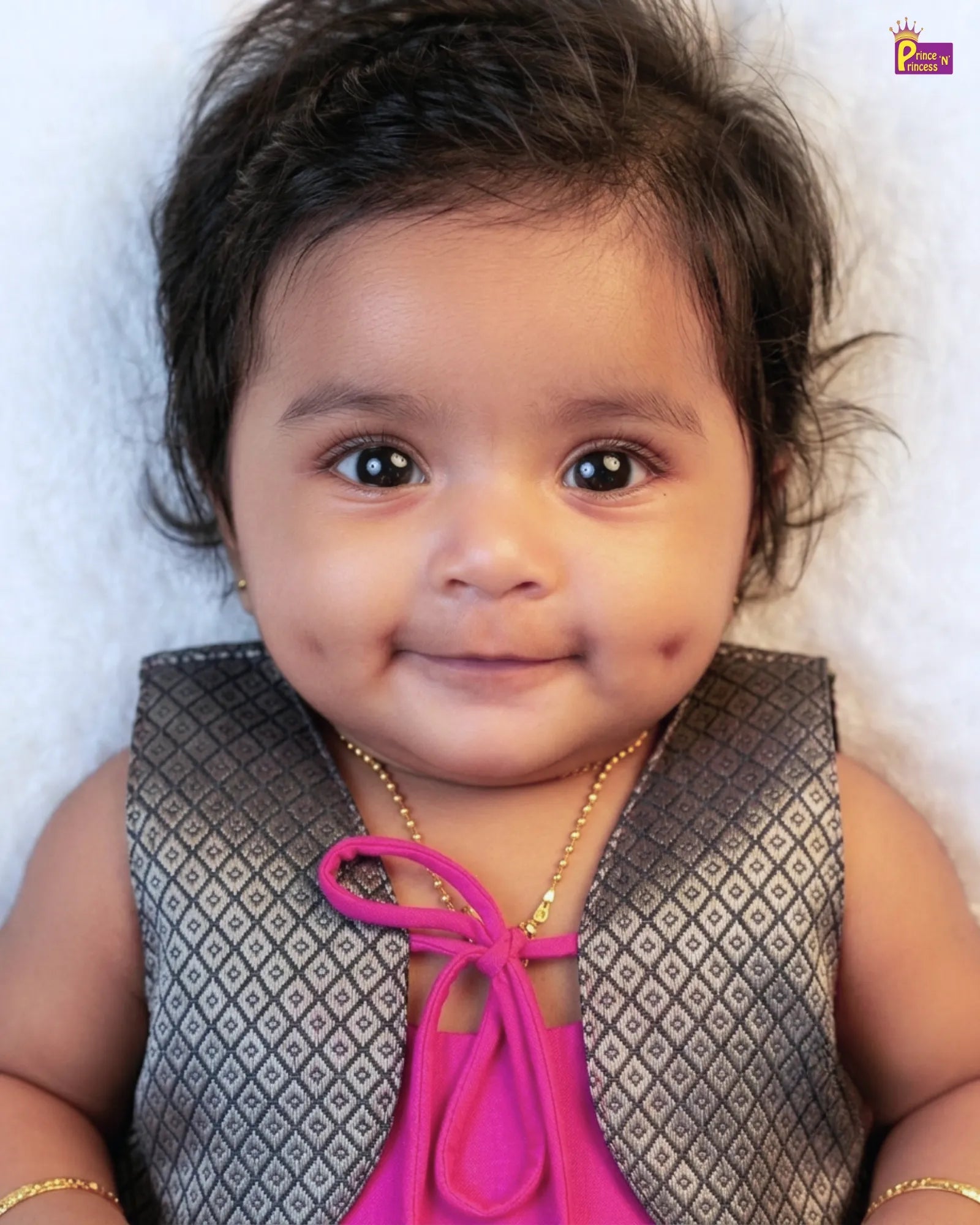 Baby wearing a patterned vest over a pink top with a white background