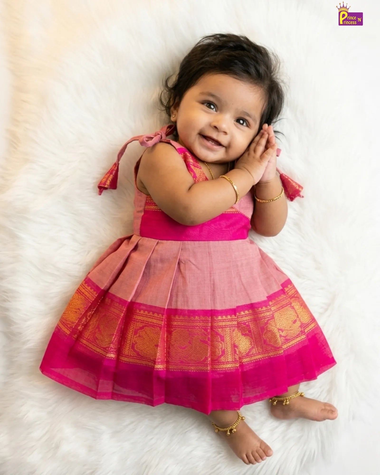 Baby in a pink traditional outfit lying on a white fluffy surface