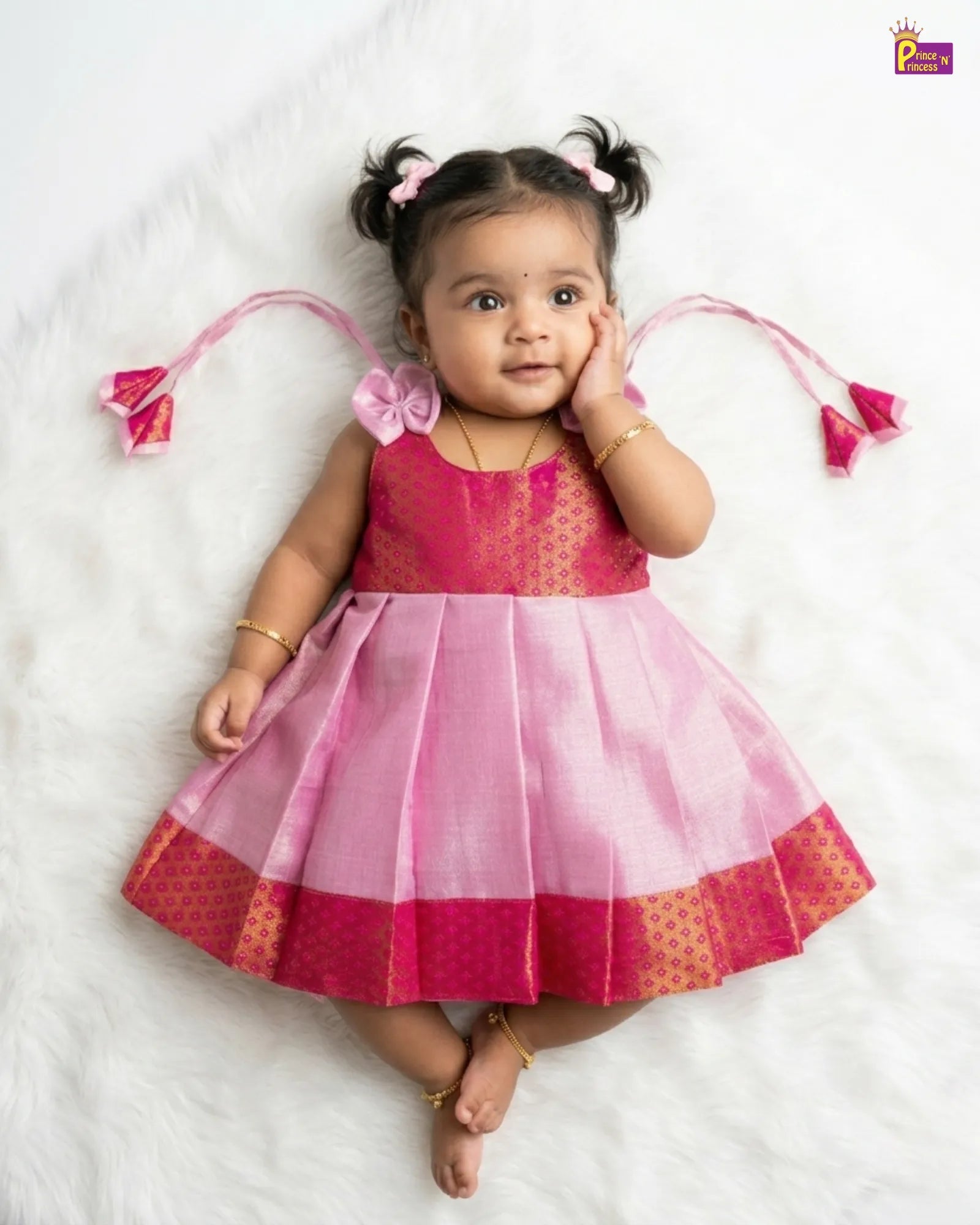 Baby wearing a pink and red traditional outfit with decorative hair accessories on a white background