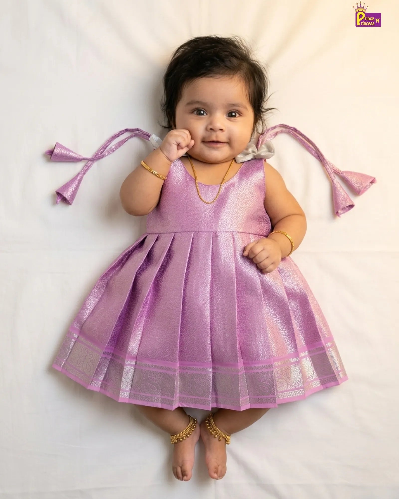 Baby wearing a pink traditional outfit with decorative ribbons on a white background