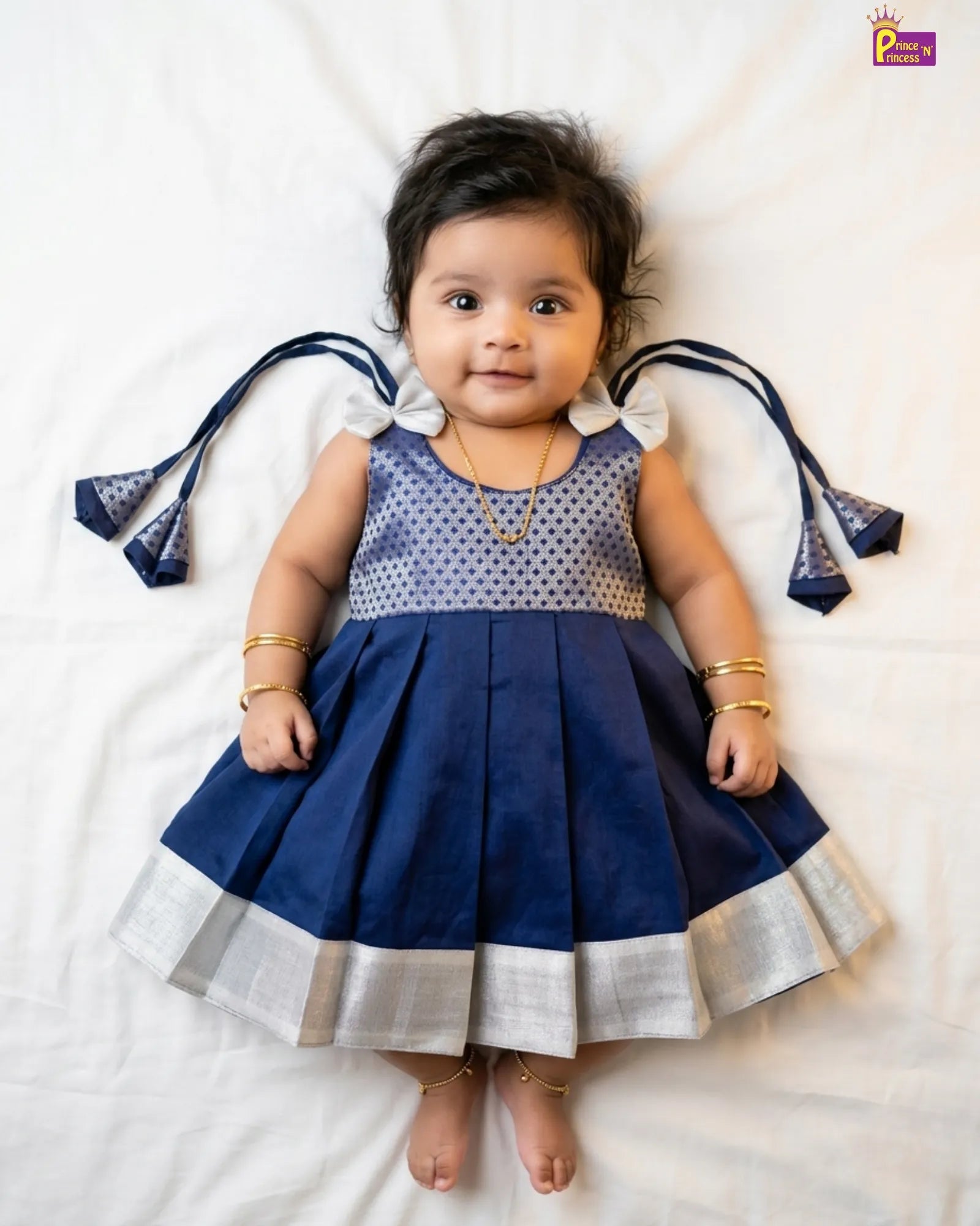 Baby wearing a blue dress with white polka dots and ribbons on a white background