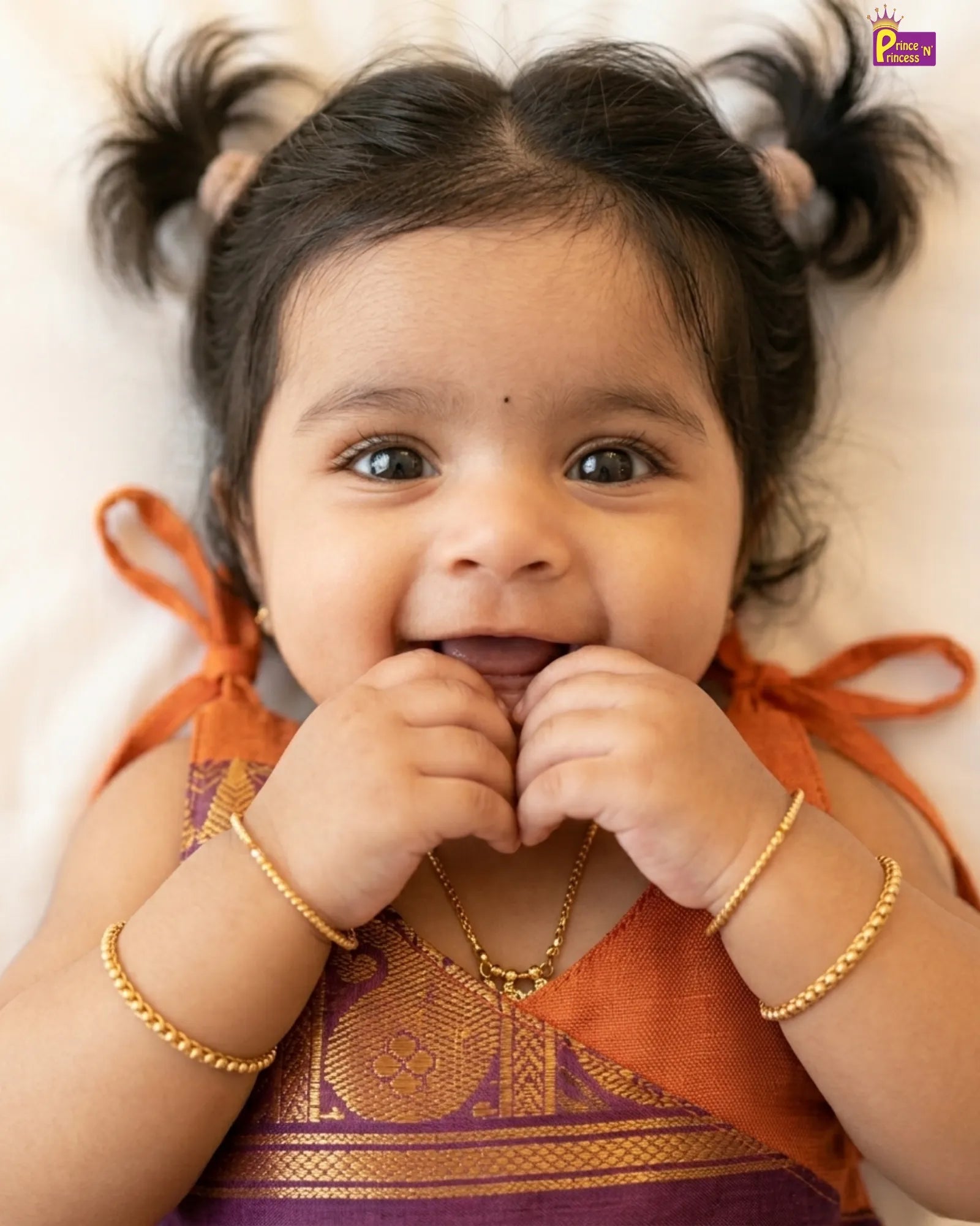 Baby wearing traditional attire with gold jewelry on a light background