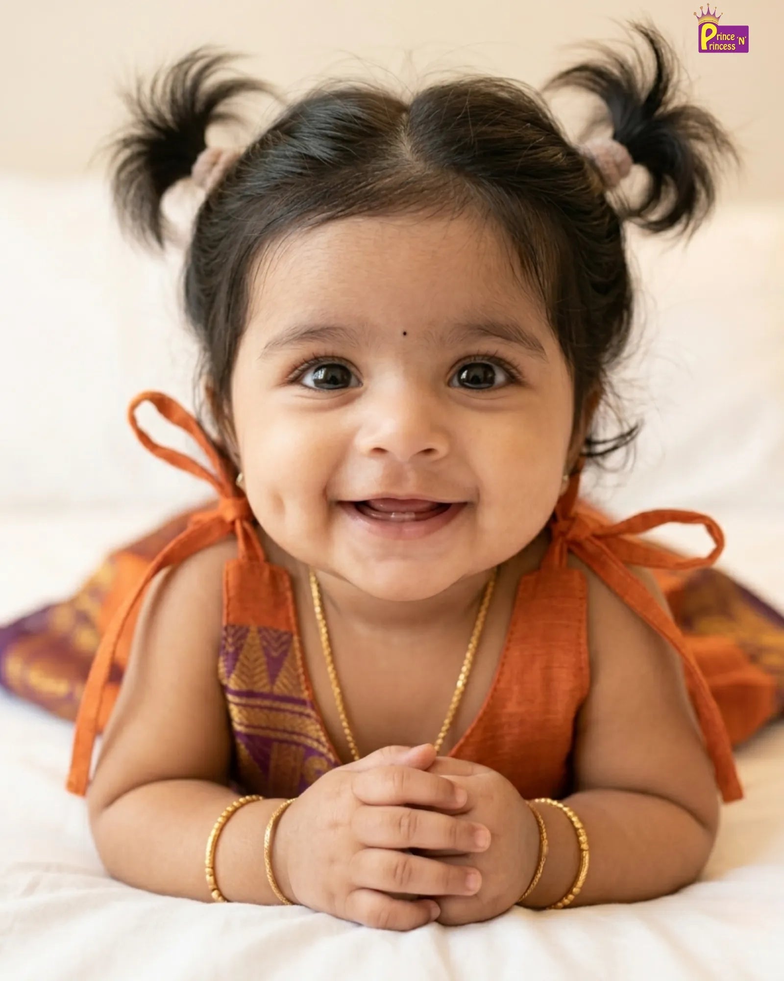 Smiling baby with pigtails wearing an orange traditional outfit on a white background