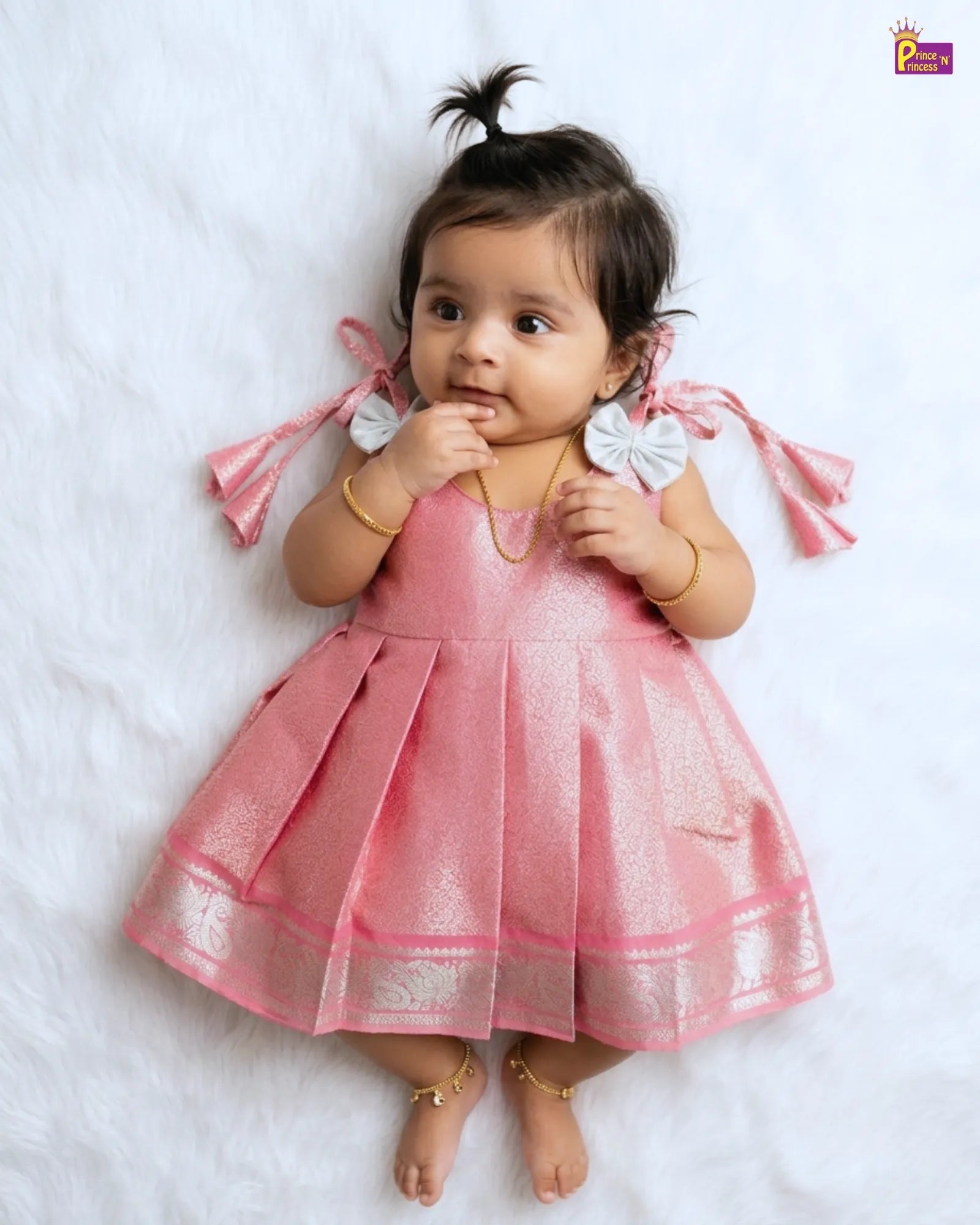 Baby wearing a pink dress with ruffled straps on a white background