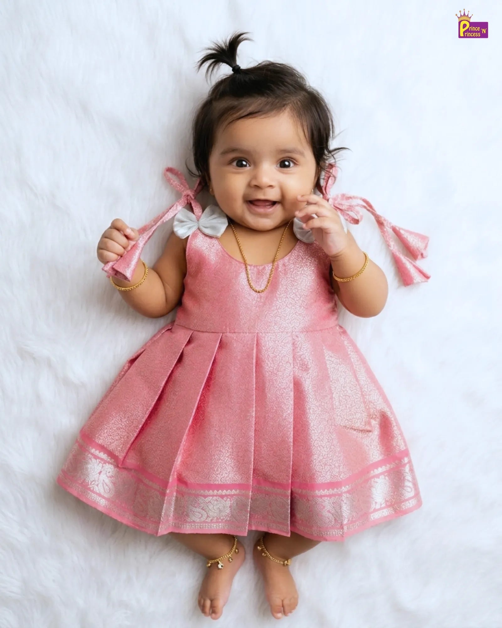 Baby in a pink dress lying on a white surface