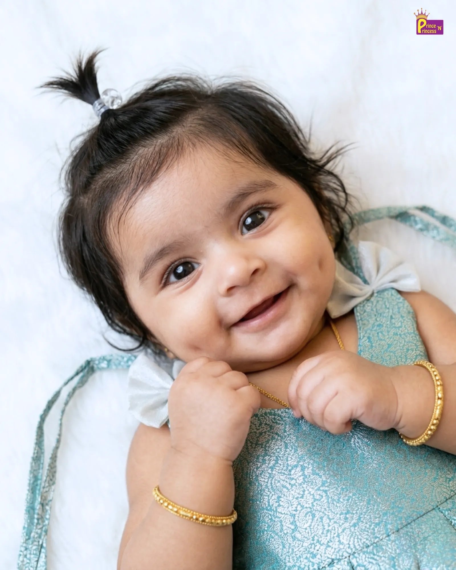 Baby wearing a blue outfit with gold bangles on a white background