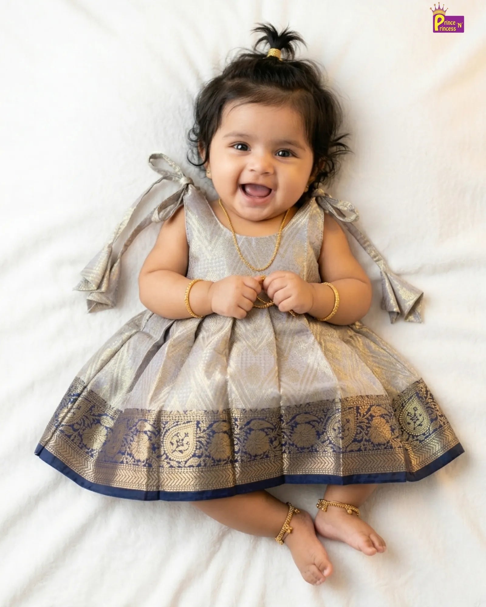Newborn baby girl in silver grey Banarasi silk frock with gold brocade weave and wide navy blue Kanjivaram zari border