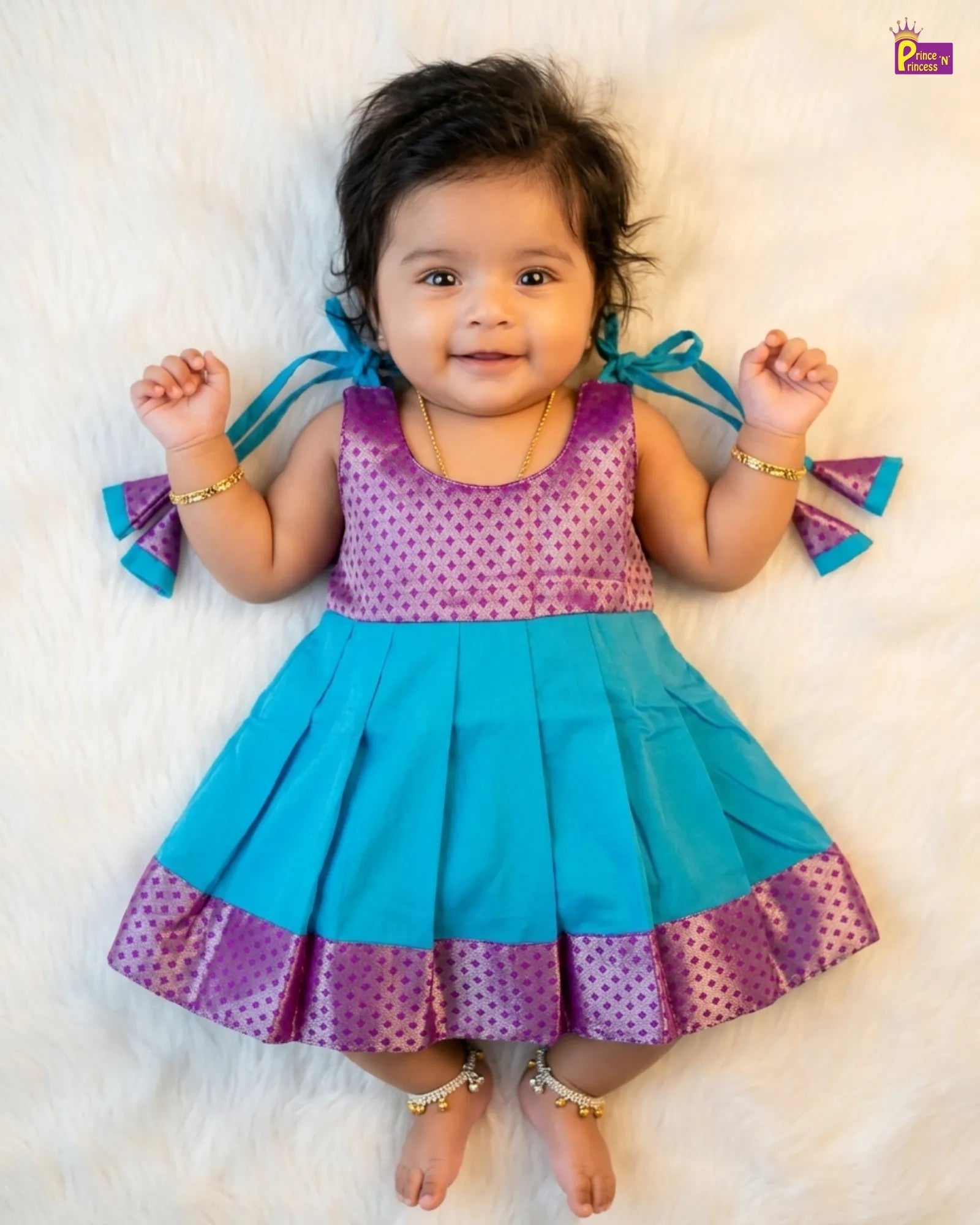 Baby wearing a colorful dress with blue and purple accents on a white background