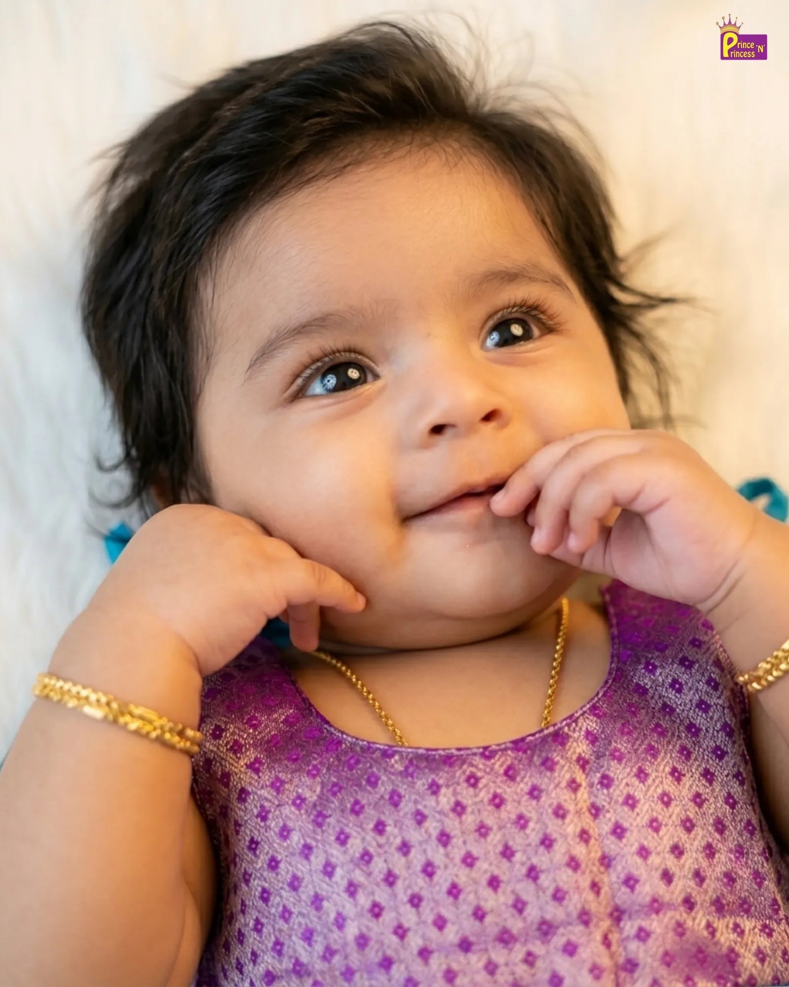 Baby wearing a purple outfit with gold jewelry on a white background