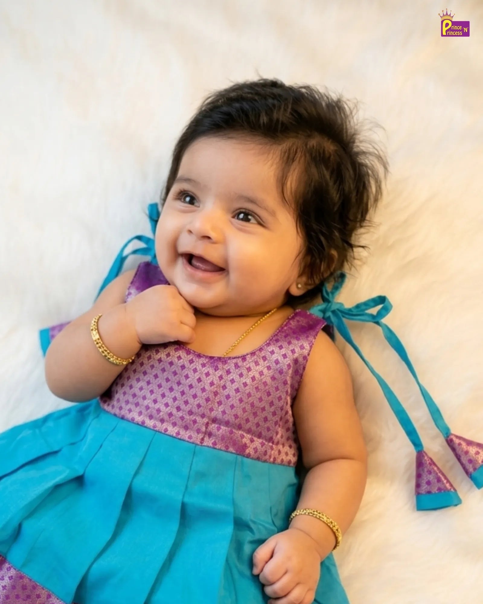 Baby wearing a purple and blue dress with a gold bracelet on a white background