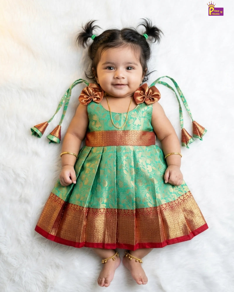 Baby wearing a green and gold traditional outfit with decorative elements on a white background