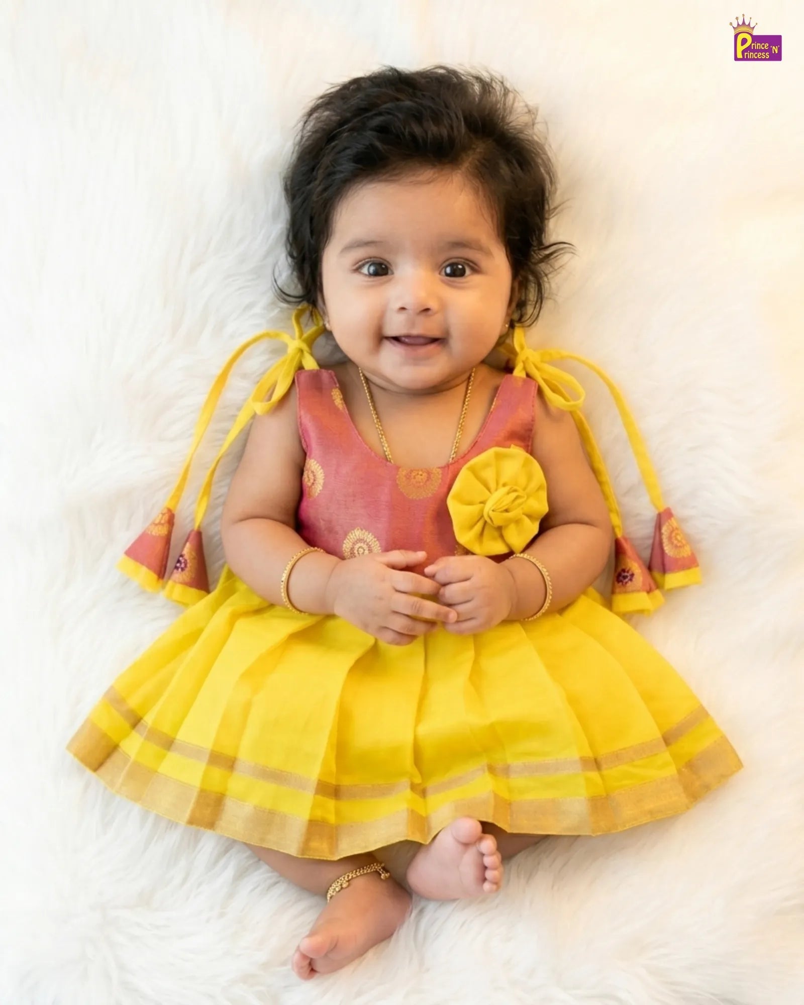 Baby in a yellow and pink dress with floral details on a white background
