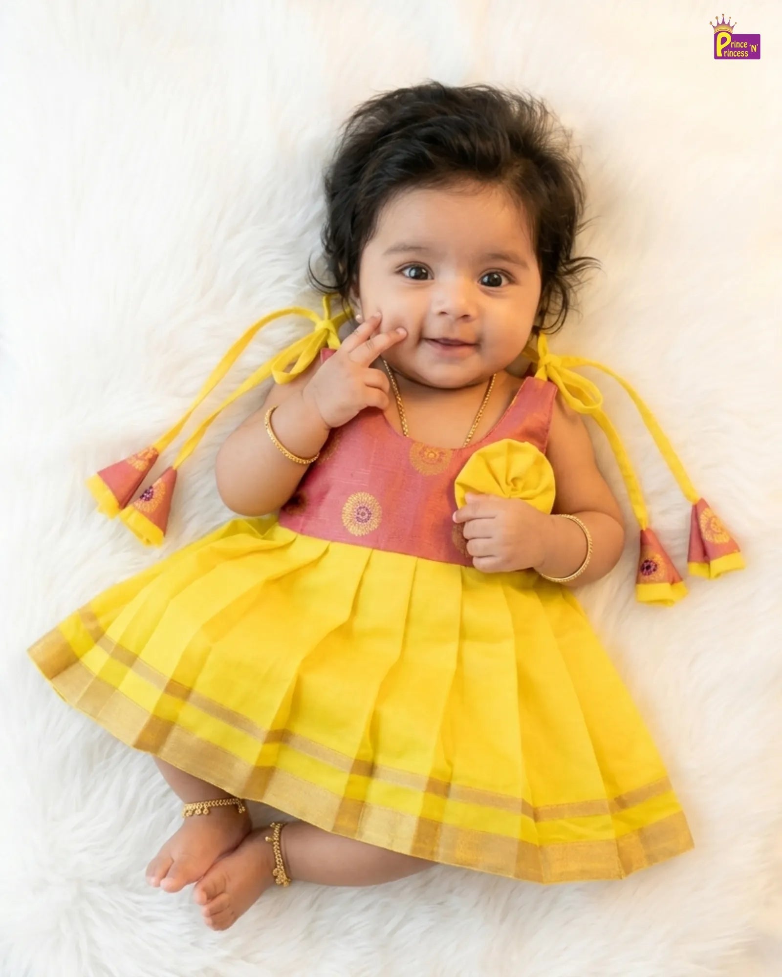 Baby wearing a yellow and pink traditional outfit on a white background