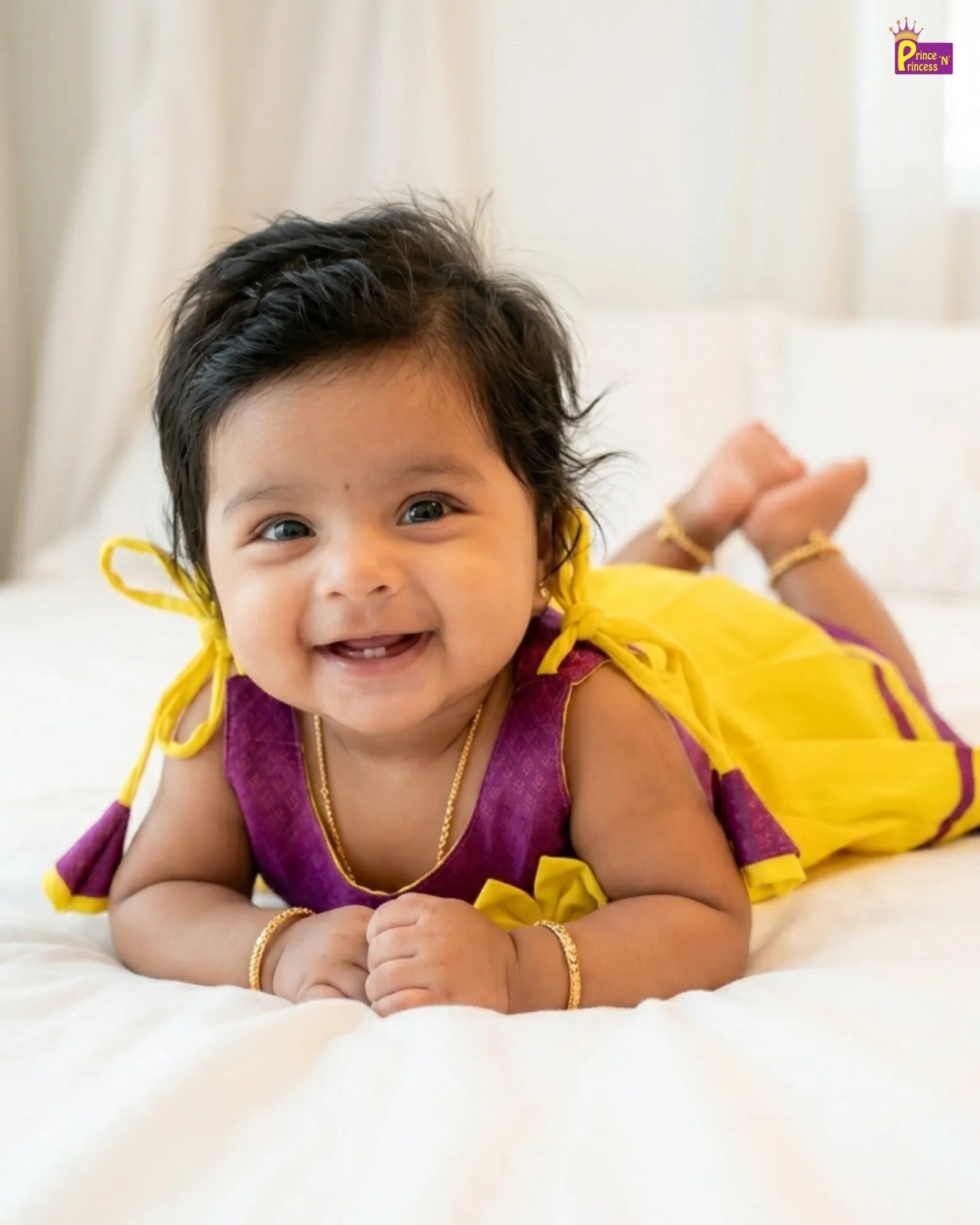 Baby in a purple and yellow outfit lying on a white surface