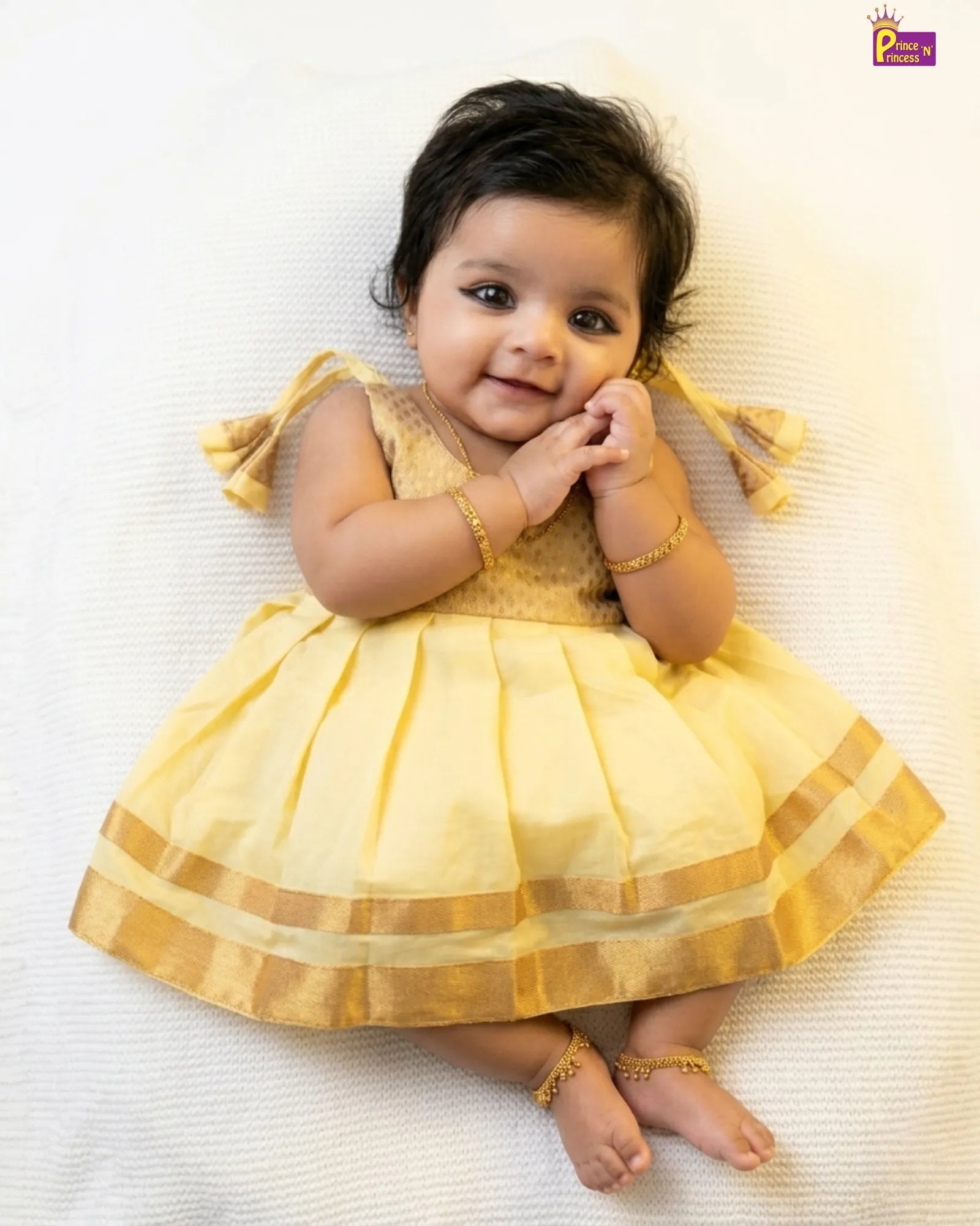 Baby in a yellow dress lying on a white surface
