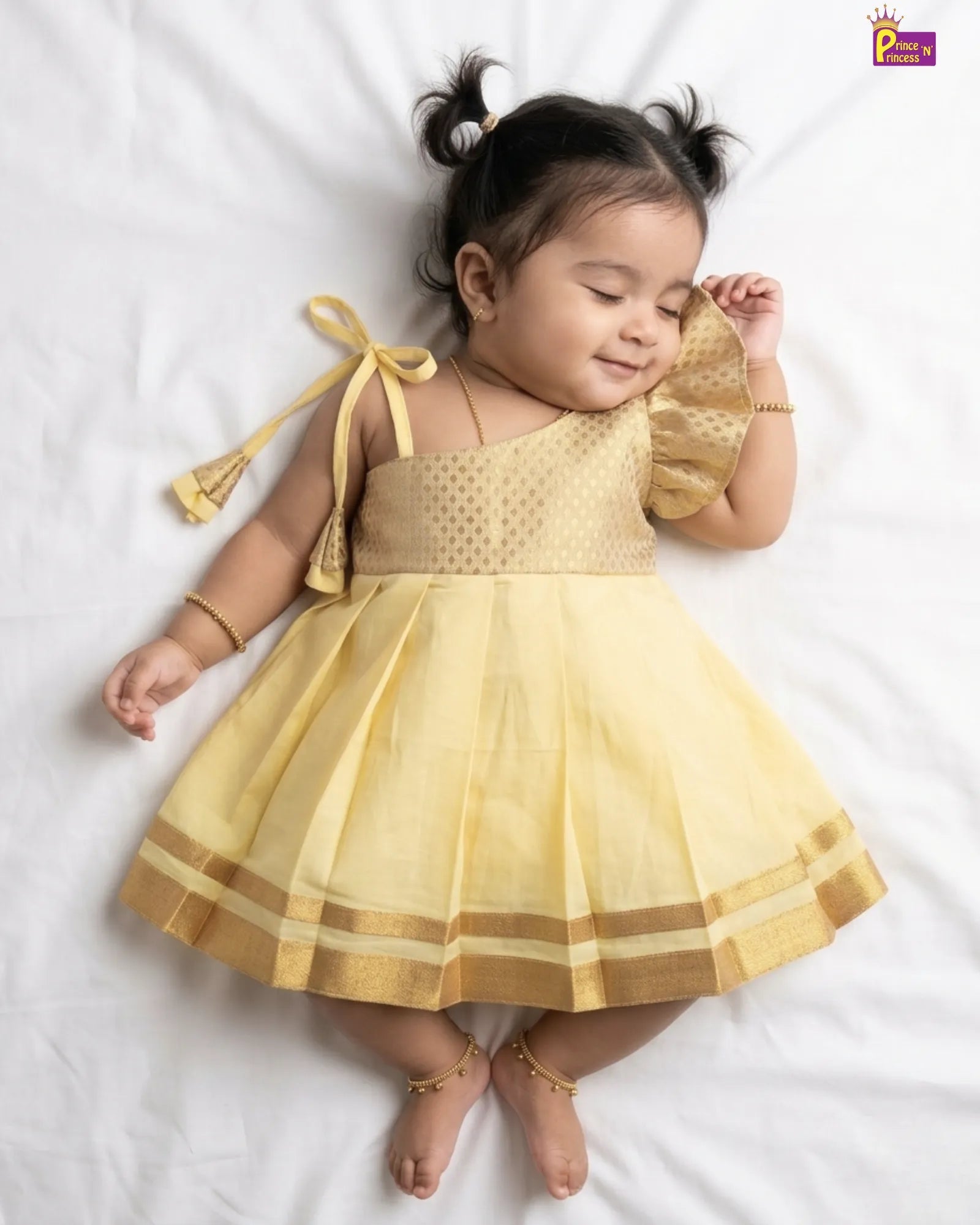 Baby in a yellow dress lying on a white surface