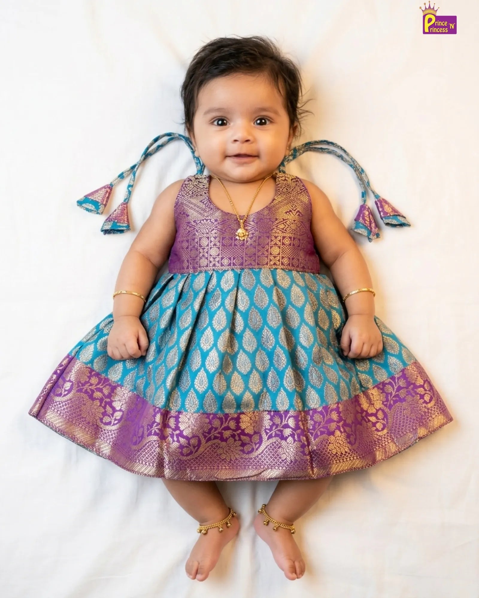Baby wearing a blue and purple traditional outfit with decorative elements on a white background