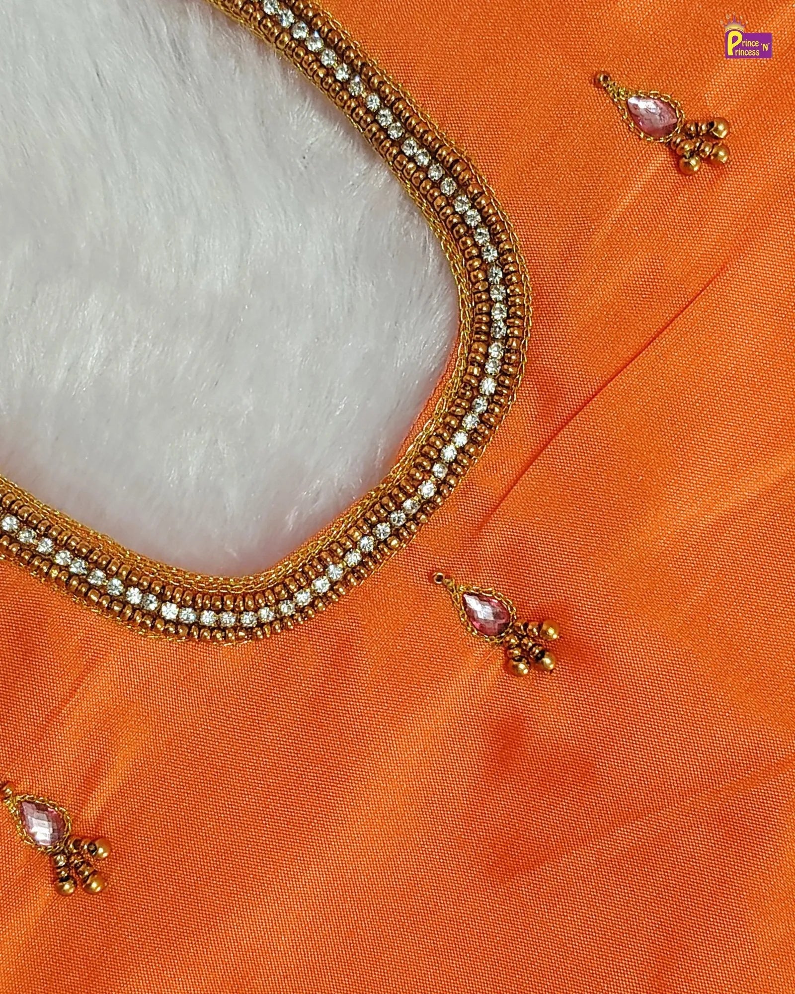 Close-up of an orange garment with gold embroidery and jewelry on a white background