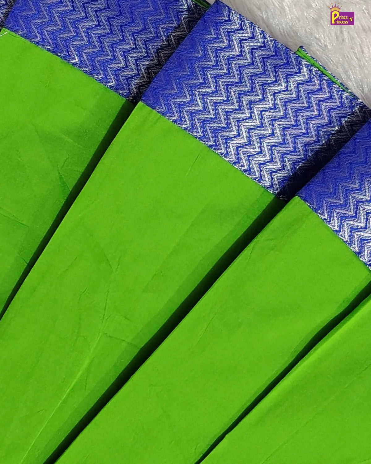 A close-up of a bright green fabric, likely a saree, featuring a blue and white woven zigzag patterned border.
