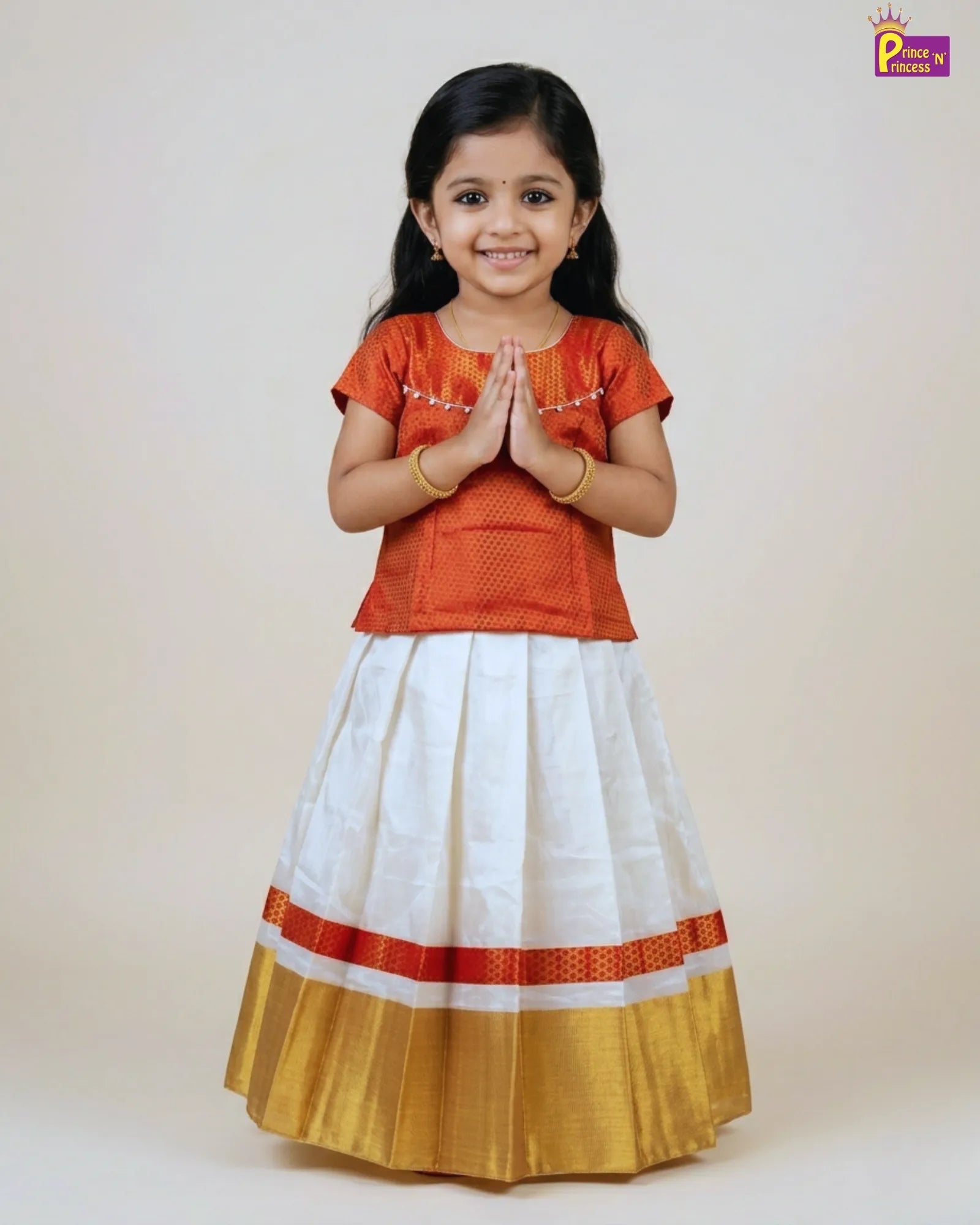 Young girl wearing a traditional outfit with an orange top and white skirt with red and gold accents on a plain background.
