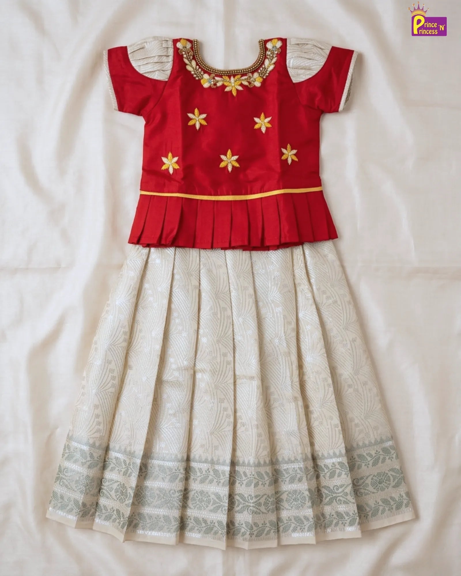 Red blouse with gold embroidery and white pleated skirt on a light background