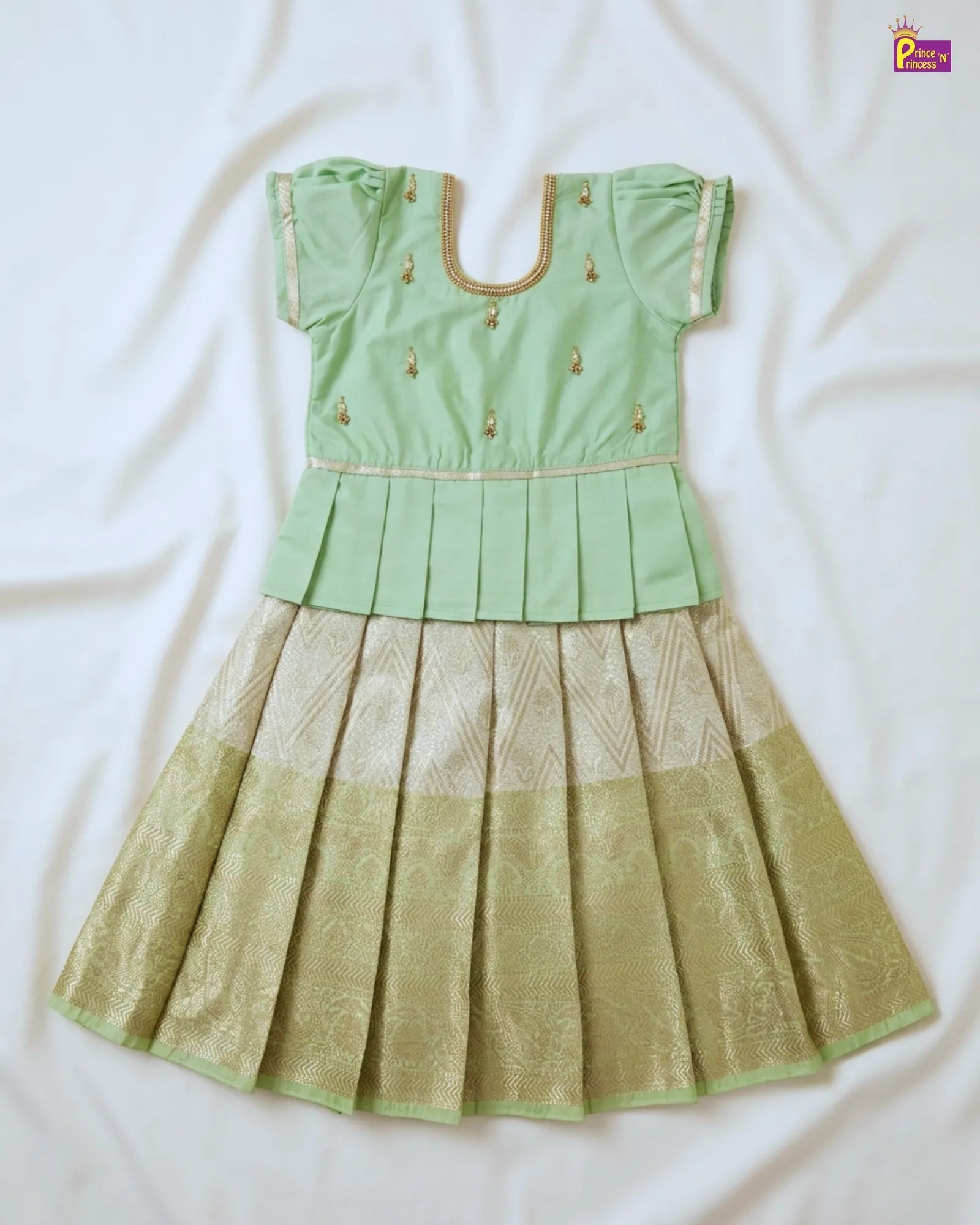Green blouse with gold embroidery and matching green and gold pleated skirt on a white background