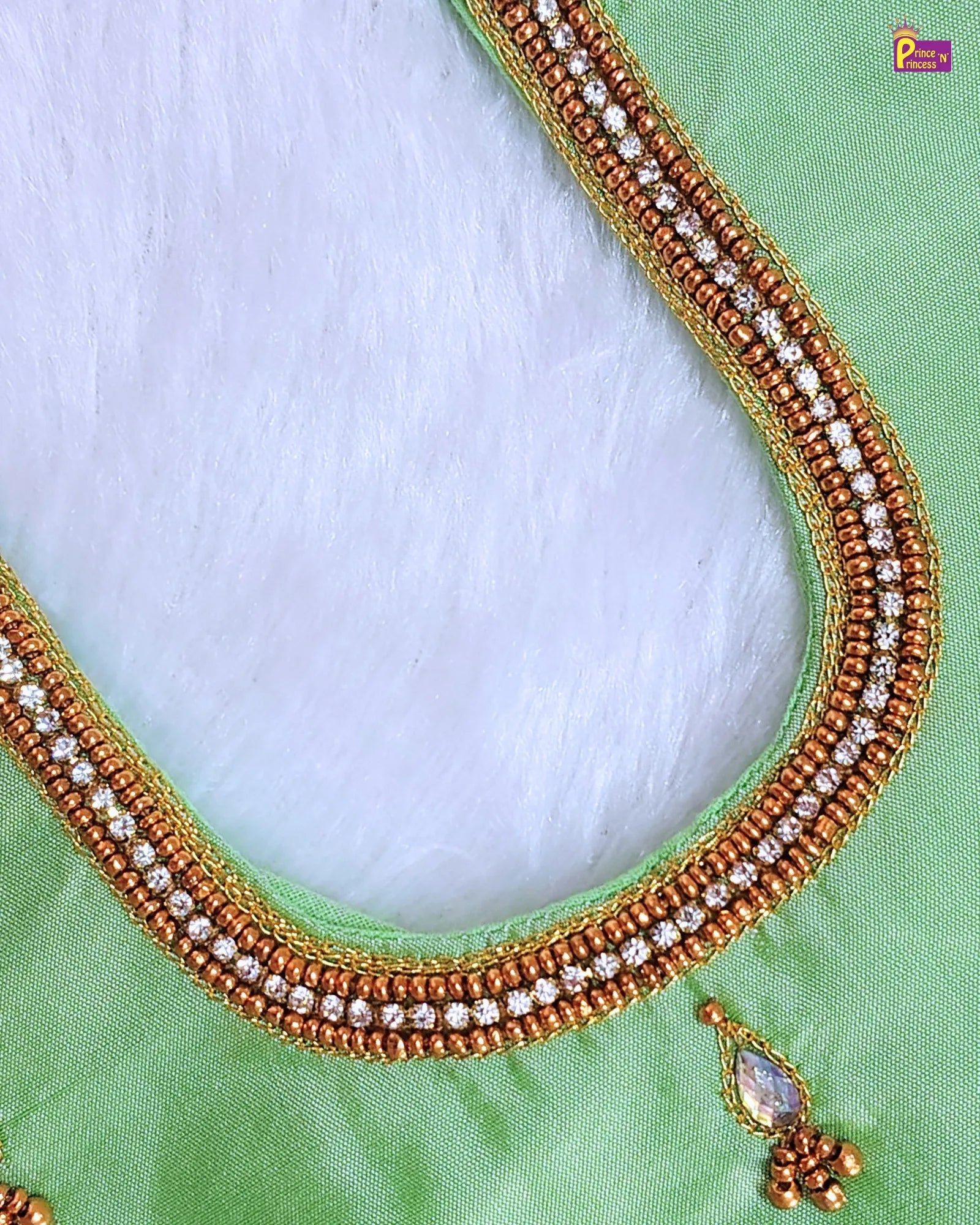 Close-up of a green blouse with gold and white beaded neckline on a light blue background.