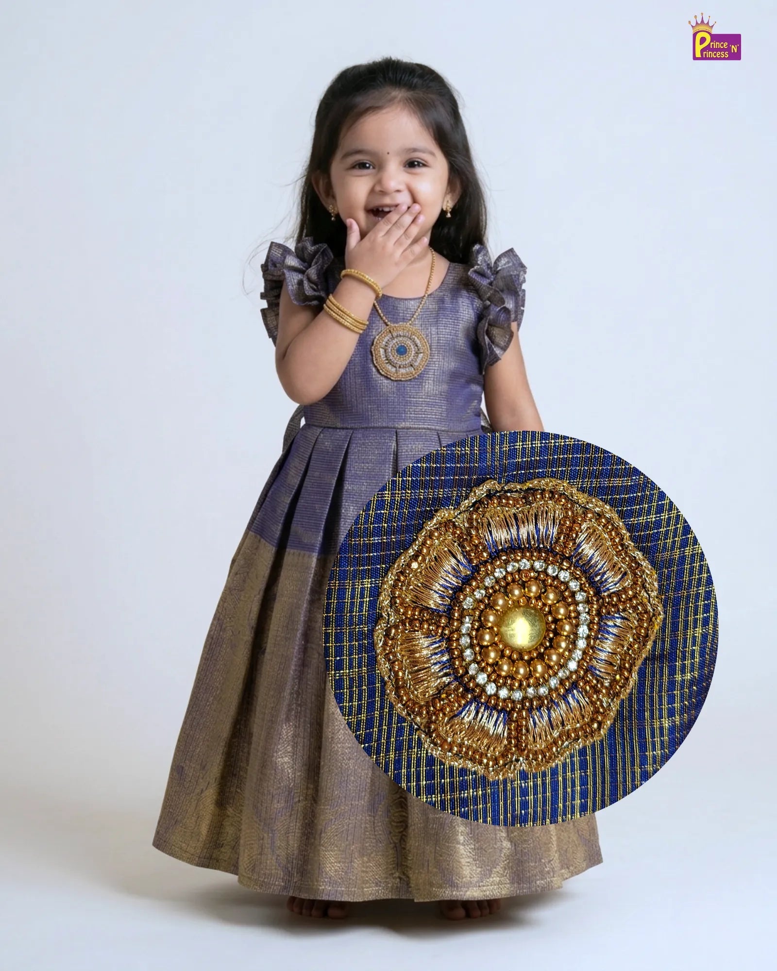 Young girl wearing a traditional outfit with a decorative gold and blue design on a white background