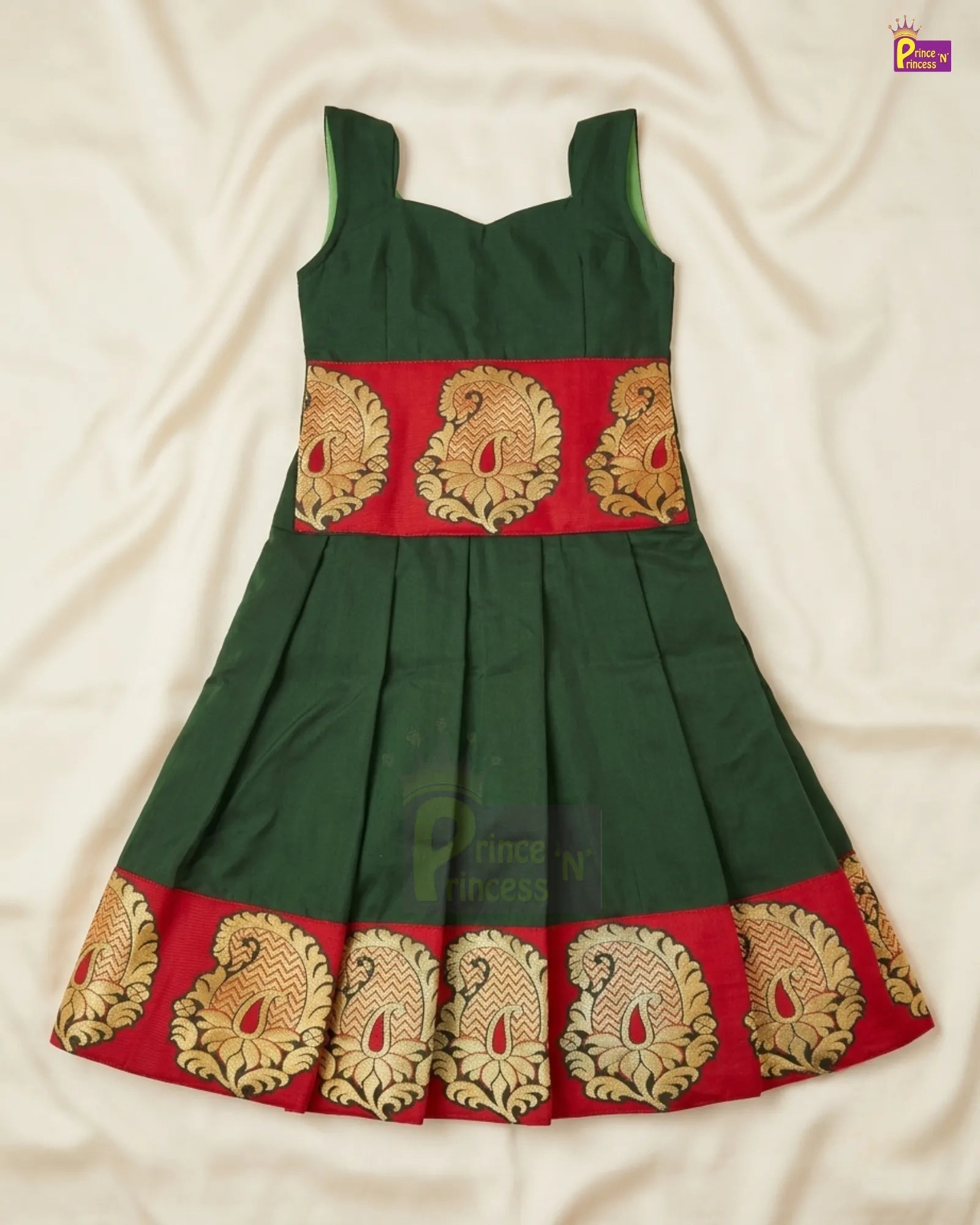 A dark green sleeveless dress with a red band featuring gold and beige peacock motifs, laid flat on a cream-colored fabric background.